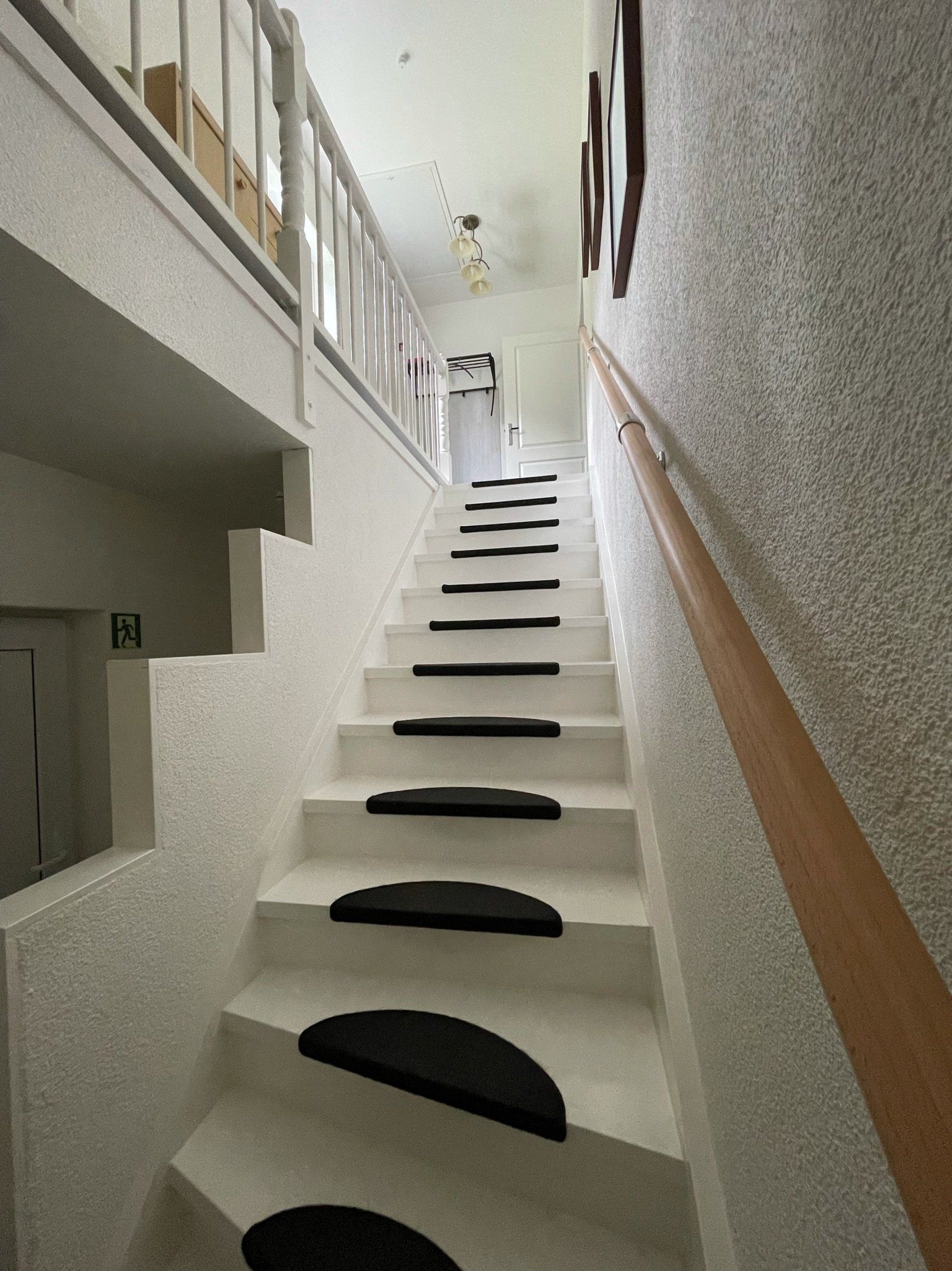 Steile Innentreppe mit schwarzen Antirutschmatten und Holzgeländer in einem schmalen Flur.