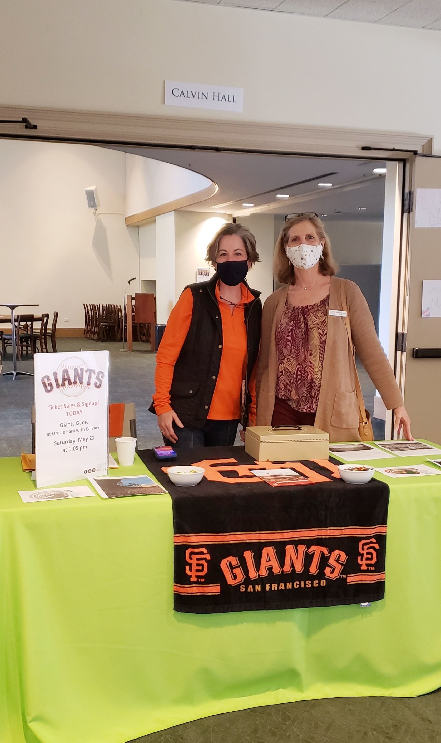 Two people standing behind a table near Calving Hall selling tickets for a Giants game