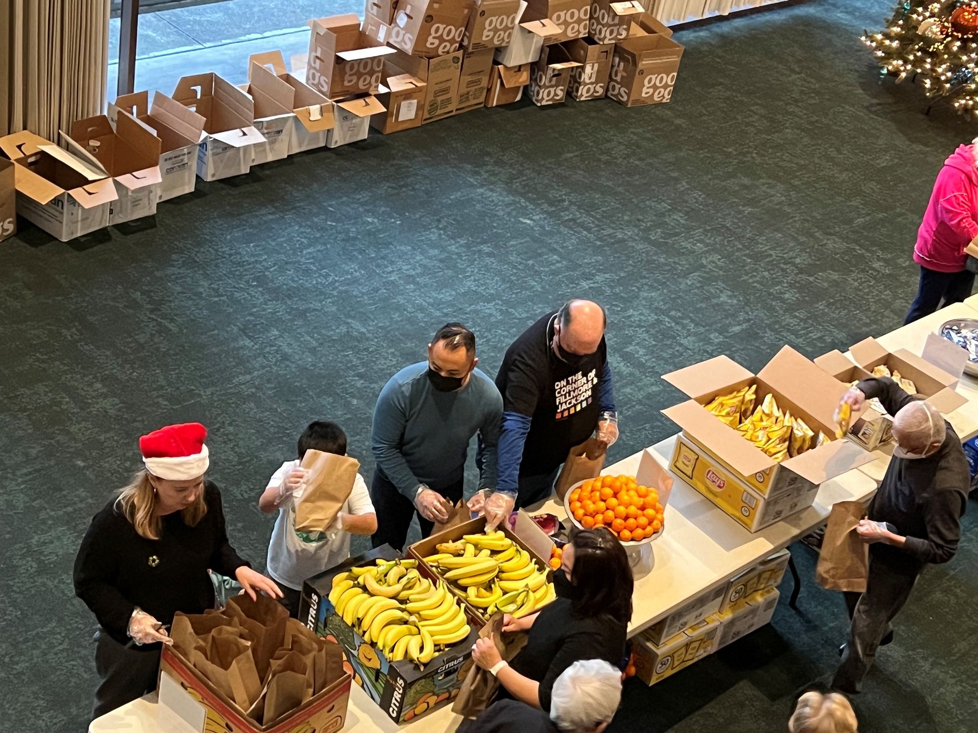 A bird's eye view of Calvary folks in Calvin Hall packing lunches during our pack-a-sack volunteer opportunity. There's a stack of boxes lined up along the wall that are waiting to have lunches be put in them.