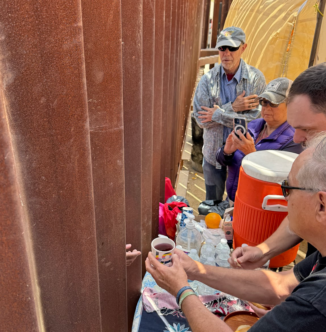 Volunteers at Whiskey 8 Humanitarian Aid site giving communion to a group of migrants on the other side of the wall, awaiting to be taken into processing from border patrol. This is during a worship service.
