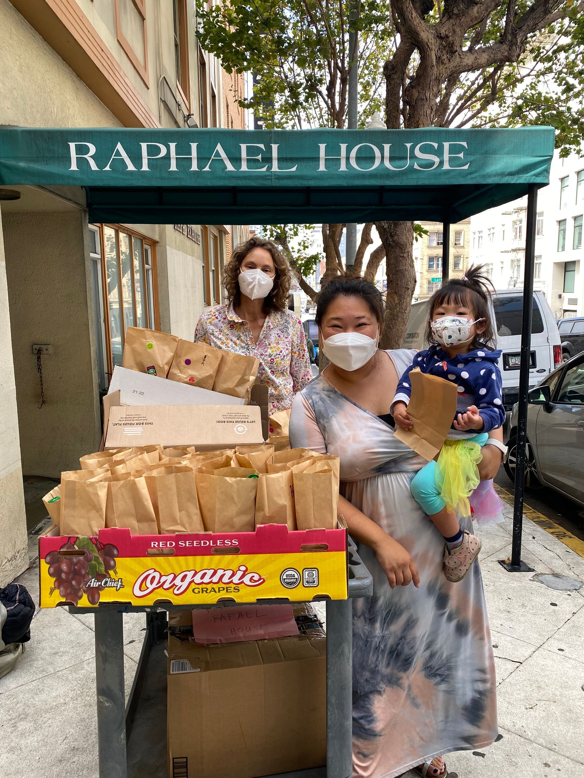 Rev. Joann Lee with her daughter and Alison Faison wheeling in a cart of packed lunches into Raphael House, one of our nonprofit partners
