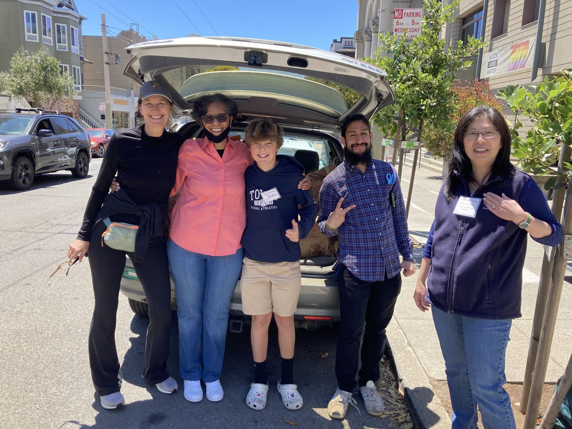 An image of volunteers packing a car full of hygiene kits for the Hope Center. They volunteers are standing under an SUV's open trunk, smiling for the camera. They are in one of the parking spaces in front of the church