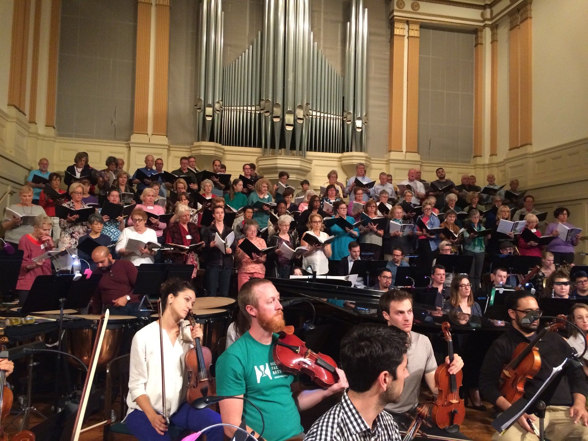 A large group of choir singers filling the choir loft. An orchestra is sitting at the forefront.