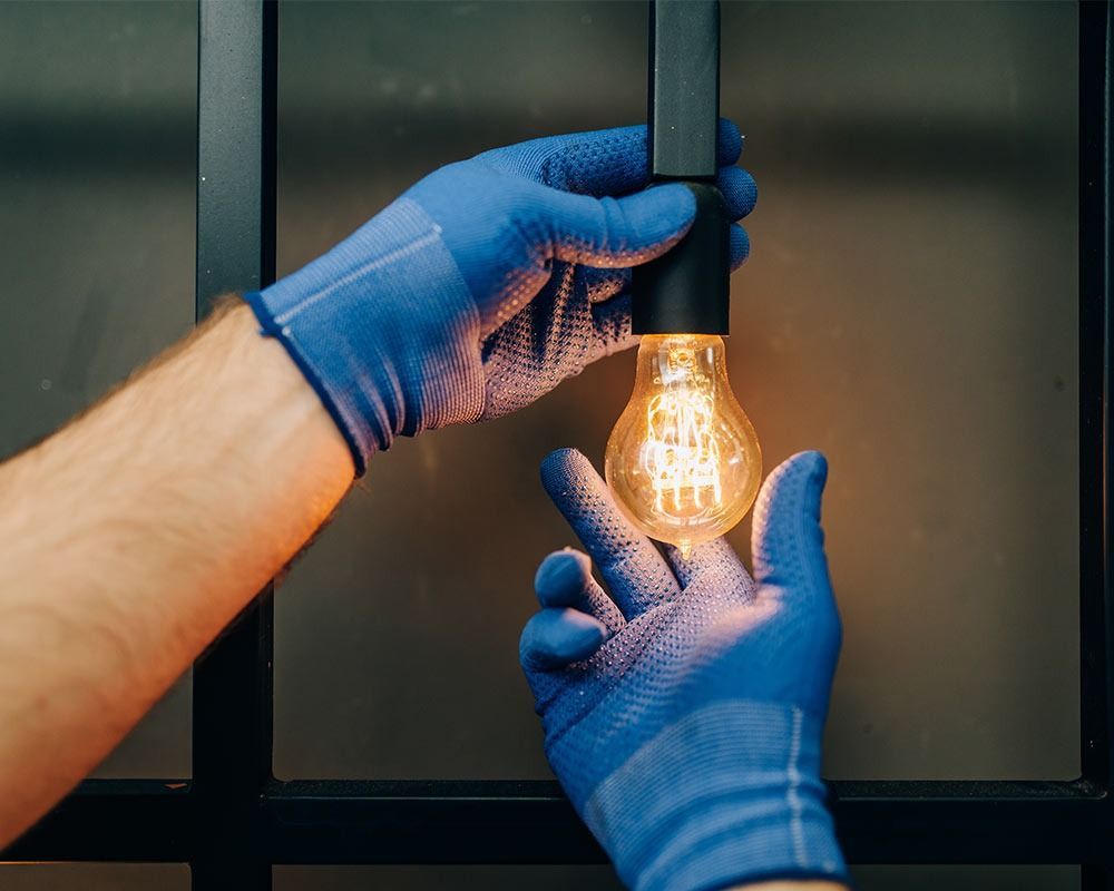 Blue-gloved hands changing a glowing light bulb in a dark fixture
