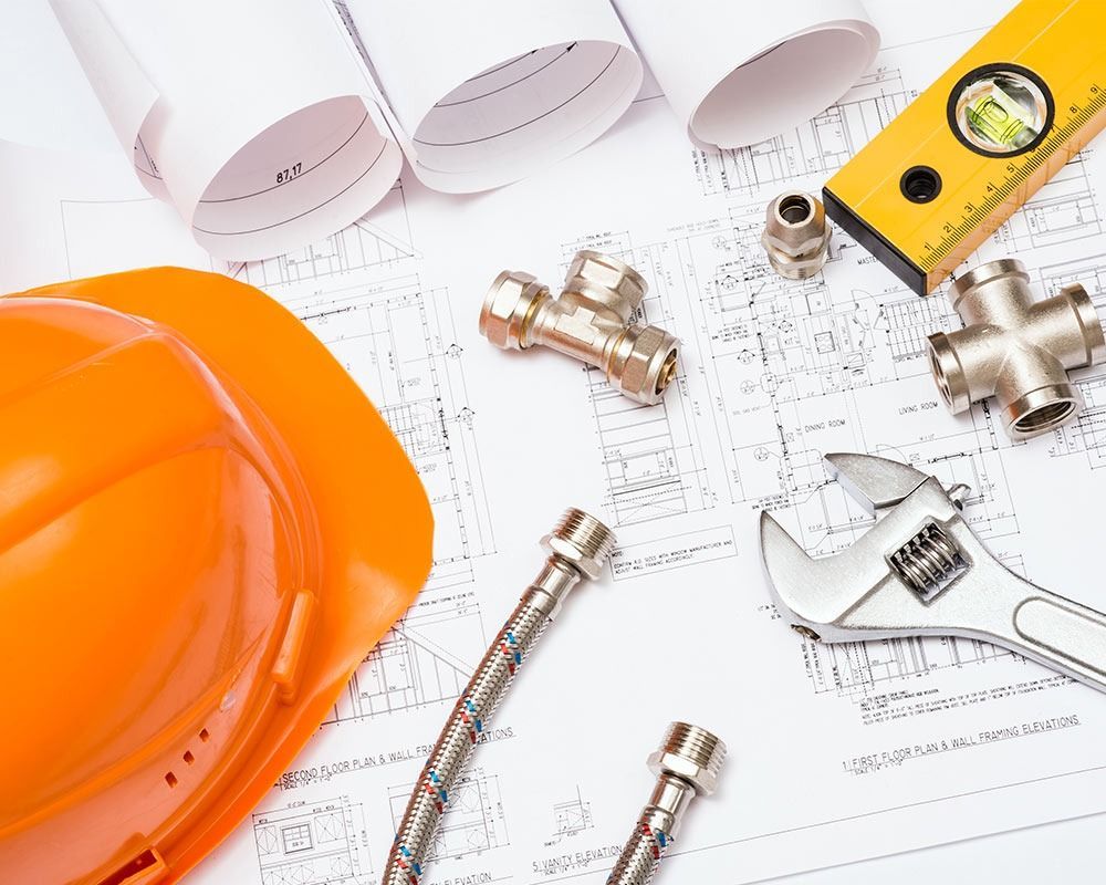 Orange hard hat, wrenches, pipe fittings, and blueprint plans on a work surface