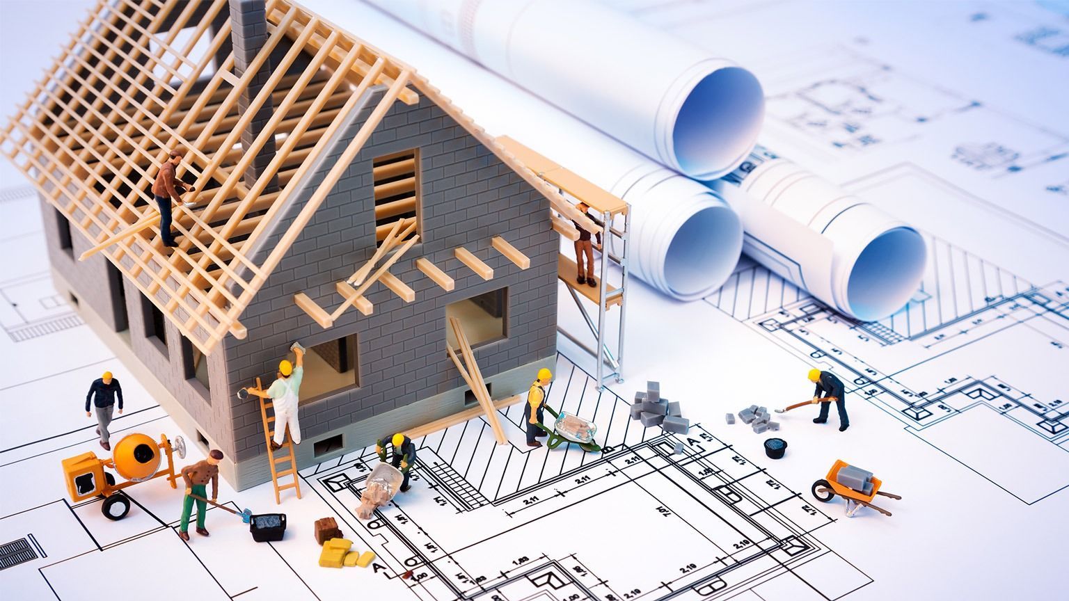 Miniature house under construction on blueprints, with workers and tools around it