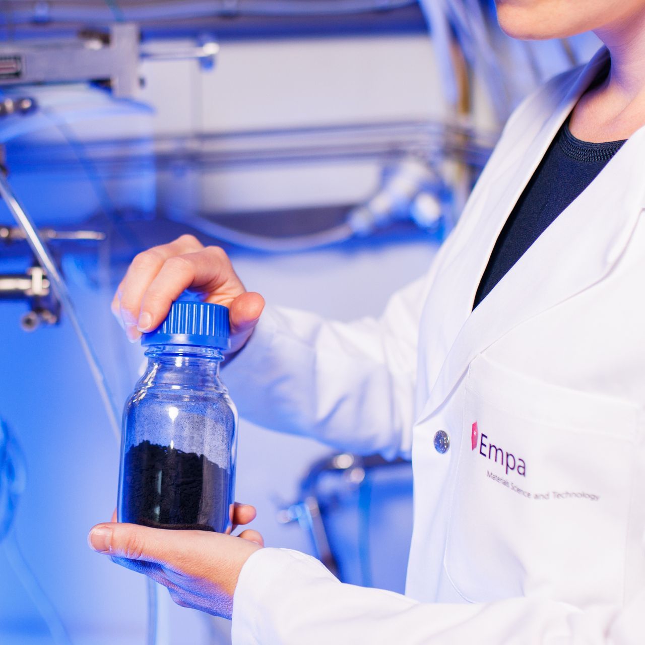 Eine Frau im Laborkittel hält eine Flasche Schwarzpulver