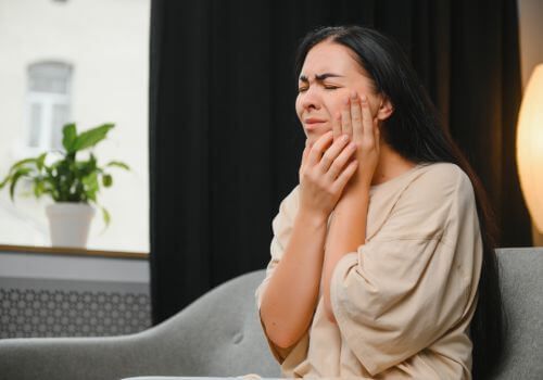 Person holding cheeks with eyes closed, sitting on a couch in a dim room.