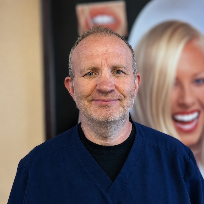 Man in navy scrubs smiling in front of a blurred salon-style poster background