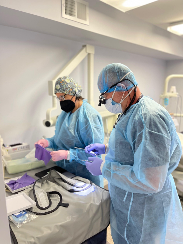 Two clinicians in blue gowns and masks preparing supplies on a hospital procedure table.