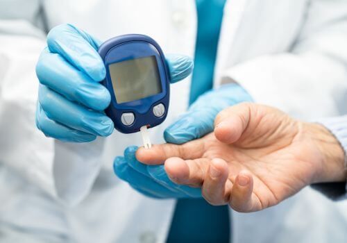 Gloved clinician checking a patient’s blood sugar with a glucometer on a finger prick