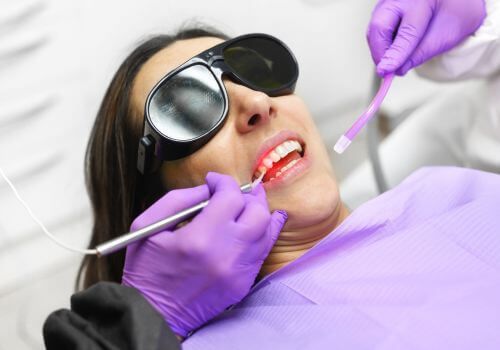 Dentist examining a patient wearing sunglasses, with purple gloves and dental tools in a clinic