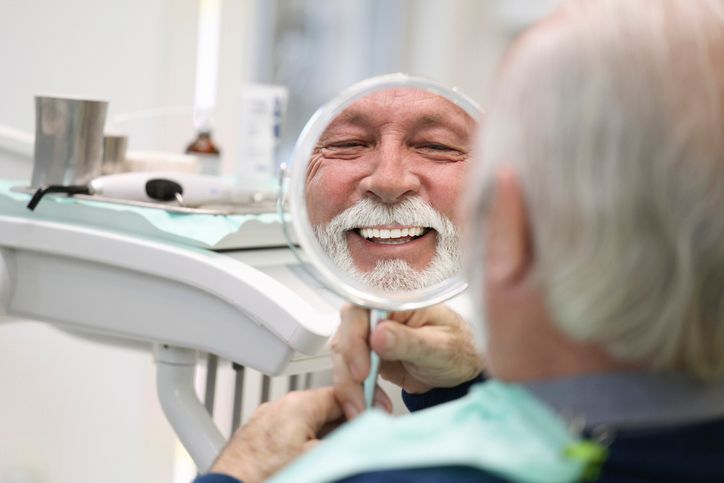 Patient smiling in dental chair while viewing their reflection in a handheld mirror