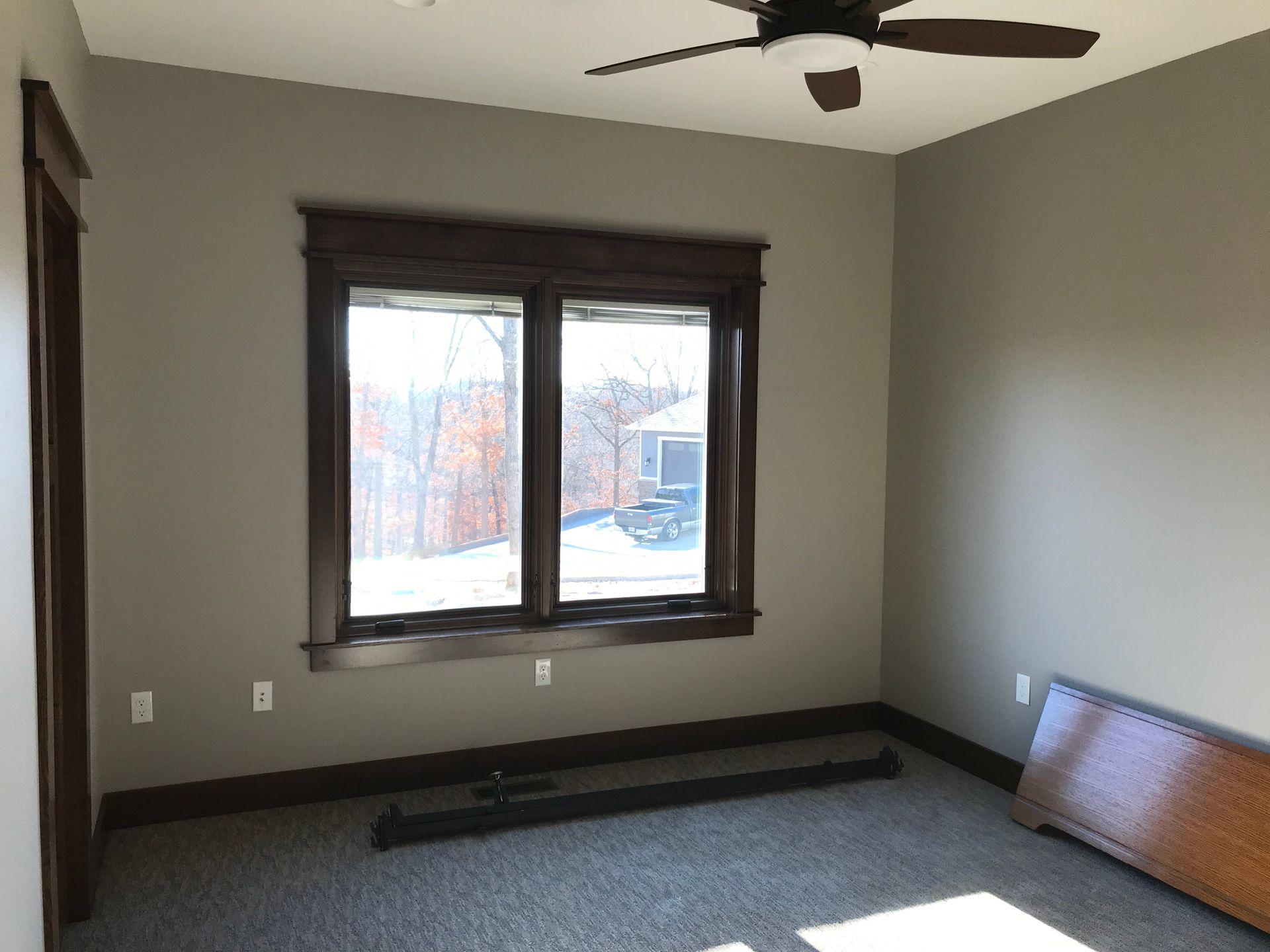 Empty bedroom with gray walls, dark trim, ceiling fan, and a window overlooking a snowy yard