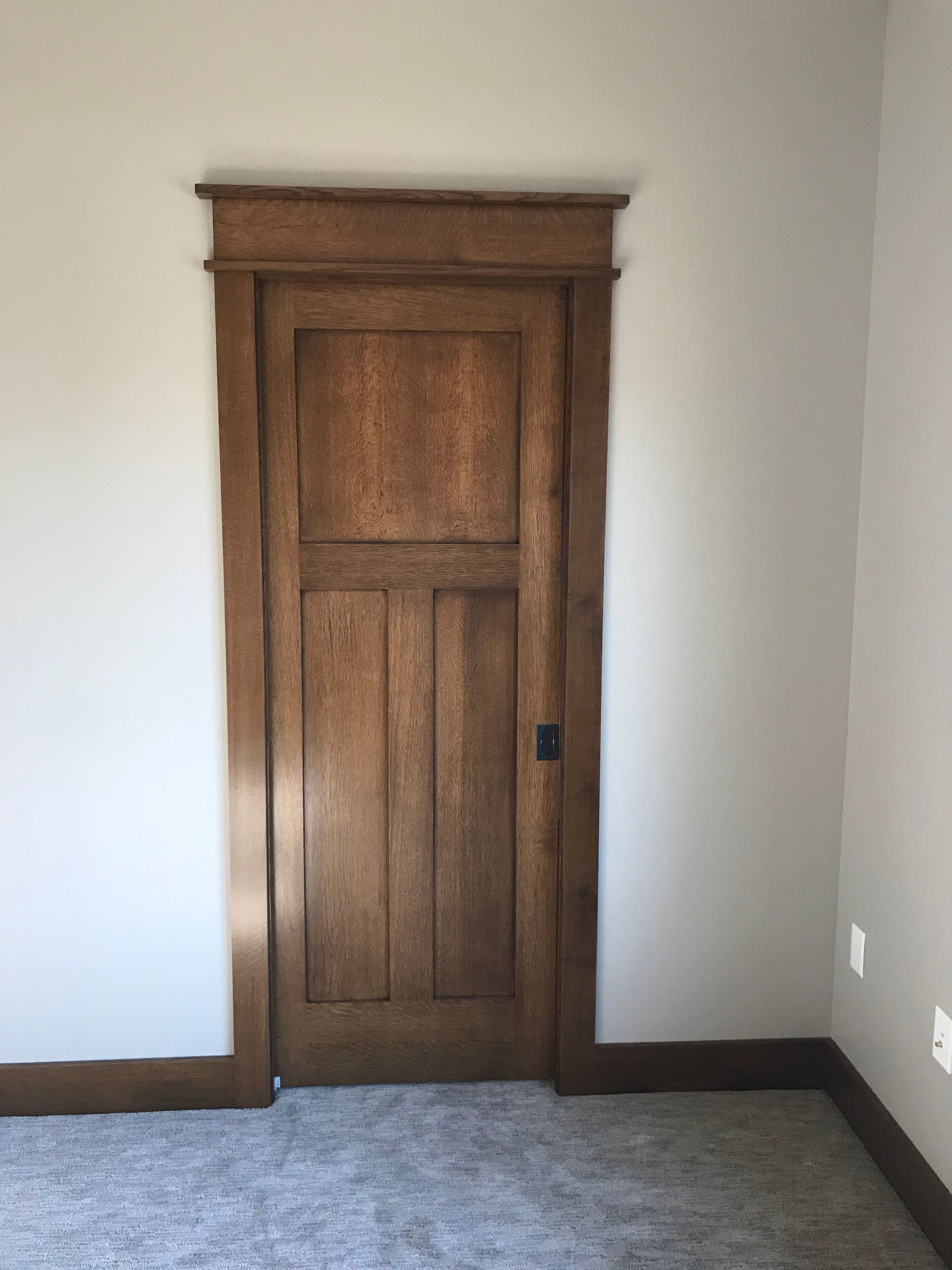 Wooden paneled closet door set in a white wall above gray carpet.