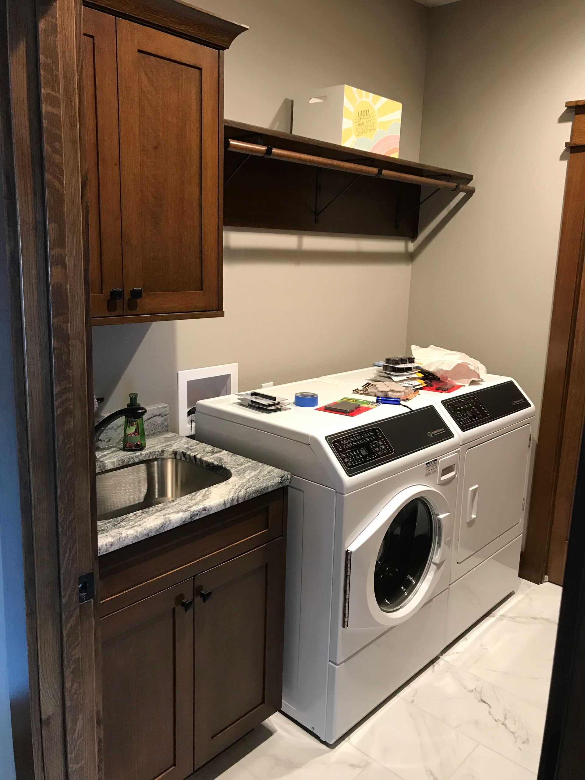 Laundry room with a top-loading washer beside a sink and dark wood cabinets.