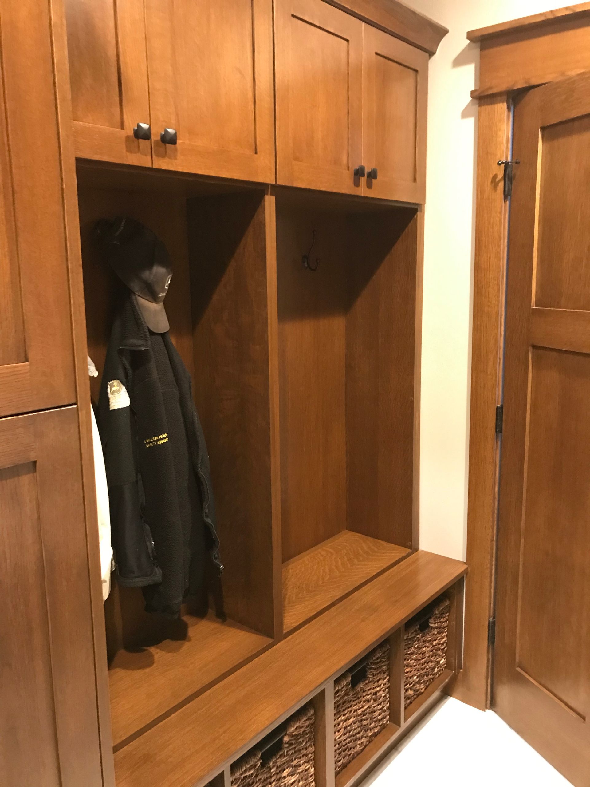 Wooden entryway built-in bench and coat closet with hanging dark coat and woven storage baskets below