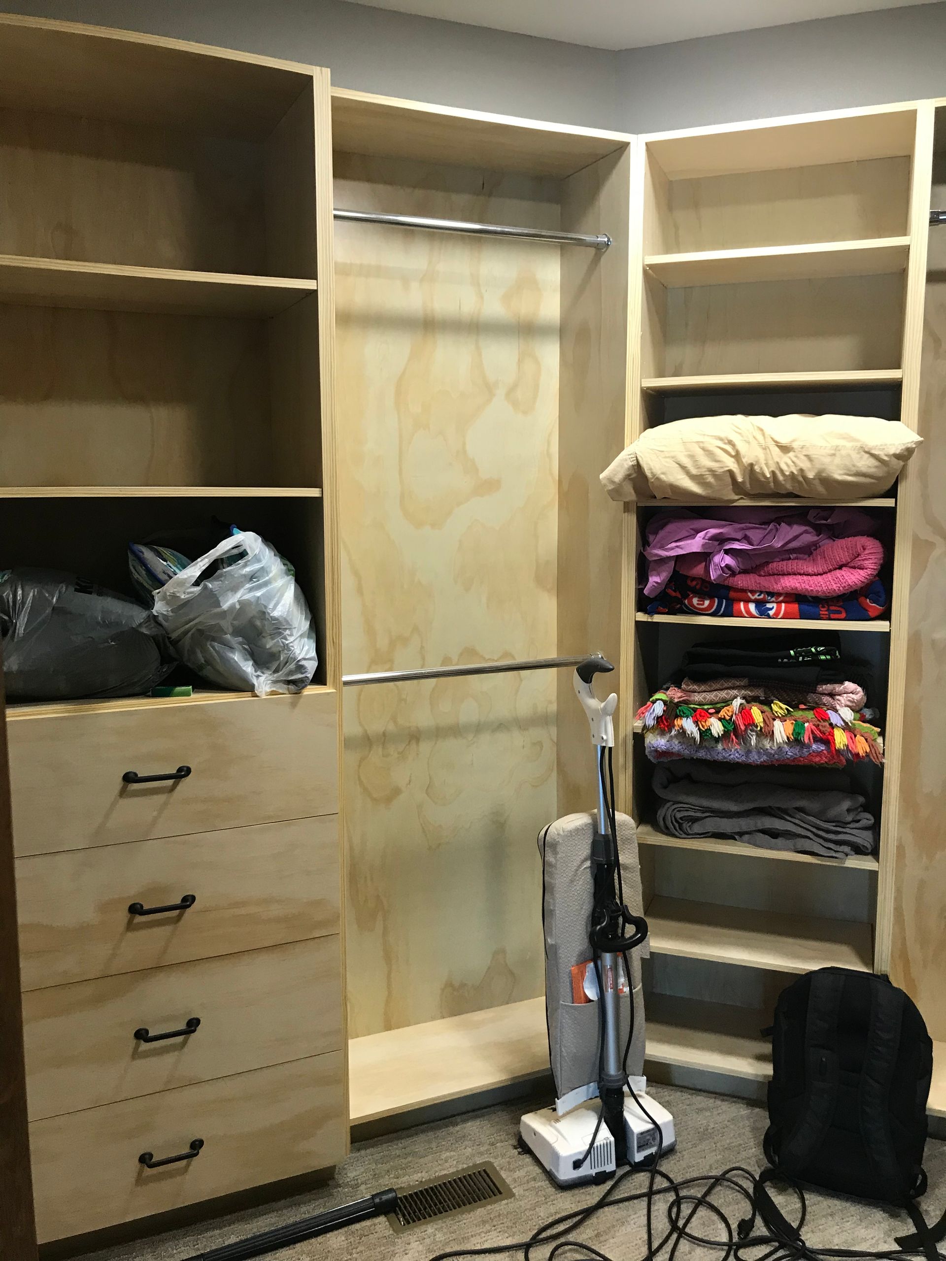 Walk-in closet with built-in shelves, drawers, hanging space, and folded clothes; vacuum in the center.