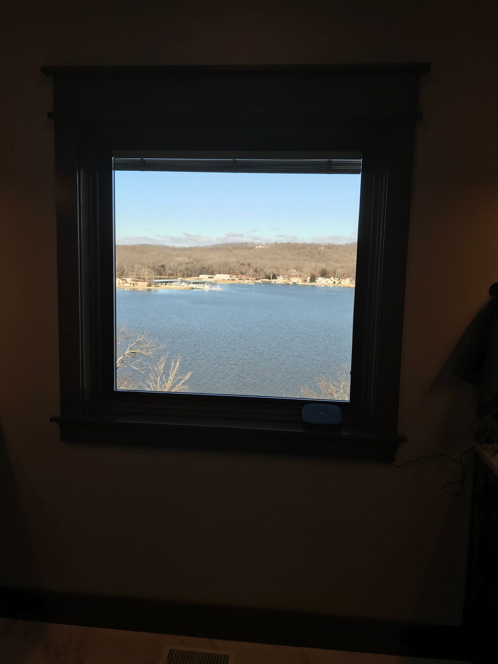 View through a dark window frame of a bright blue lake and distant shoreline in daylight