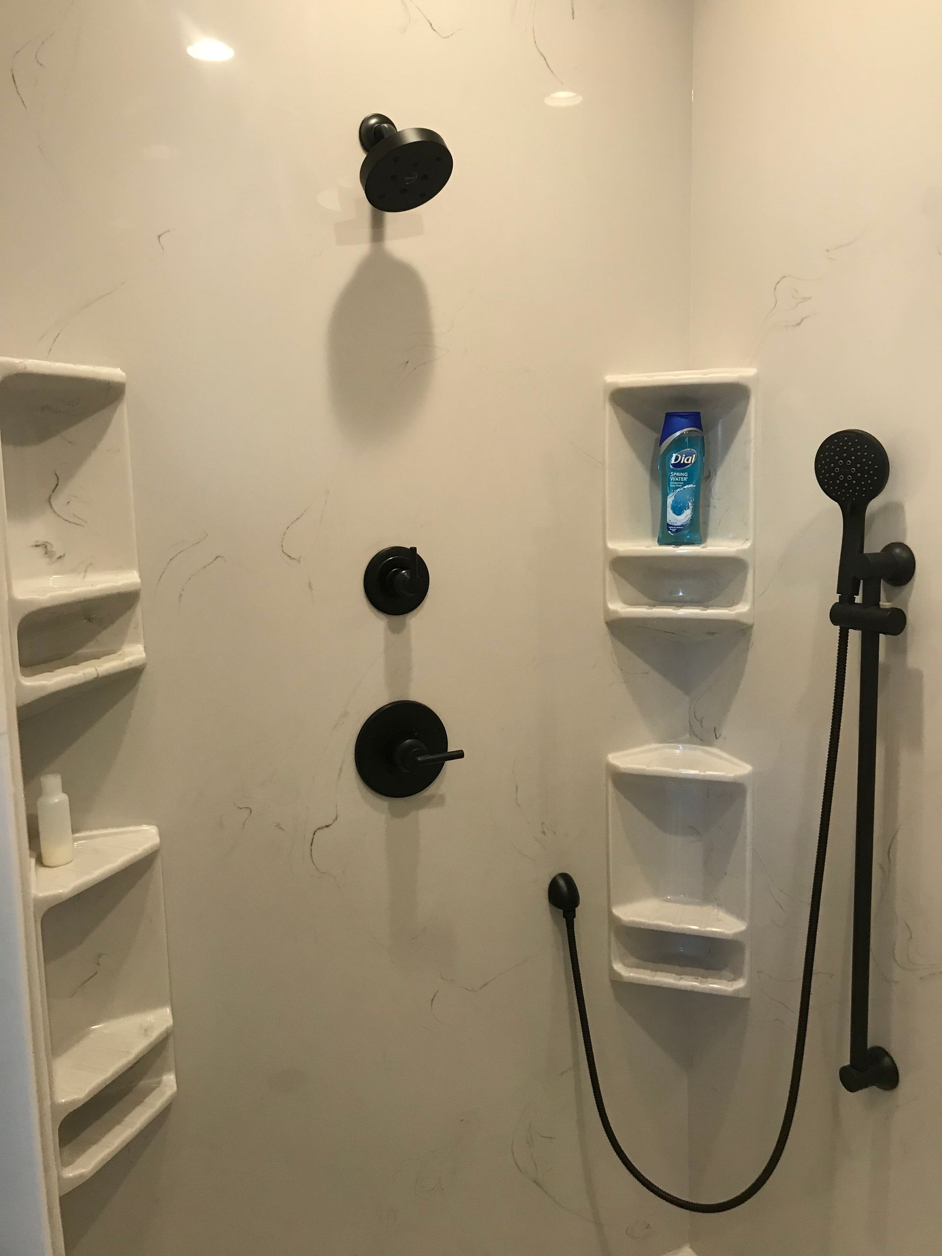 White shower with black fixtures, built-in corner shelves, and a hanging handheld showerhead.