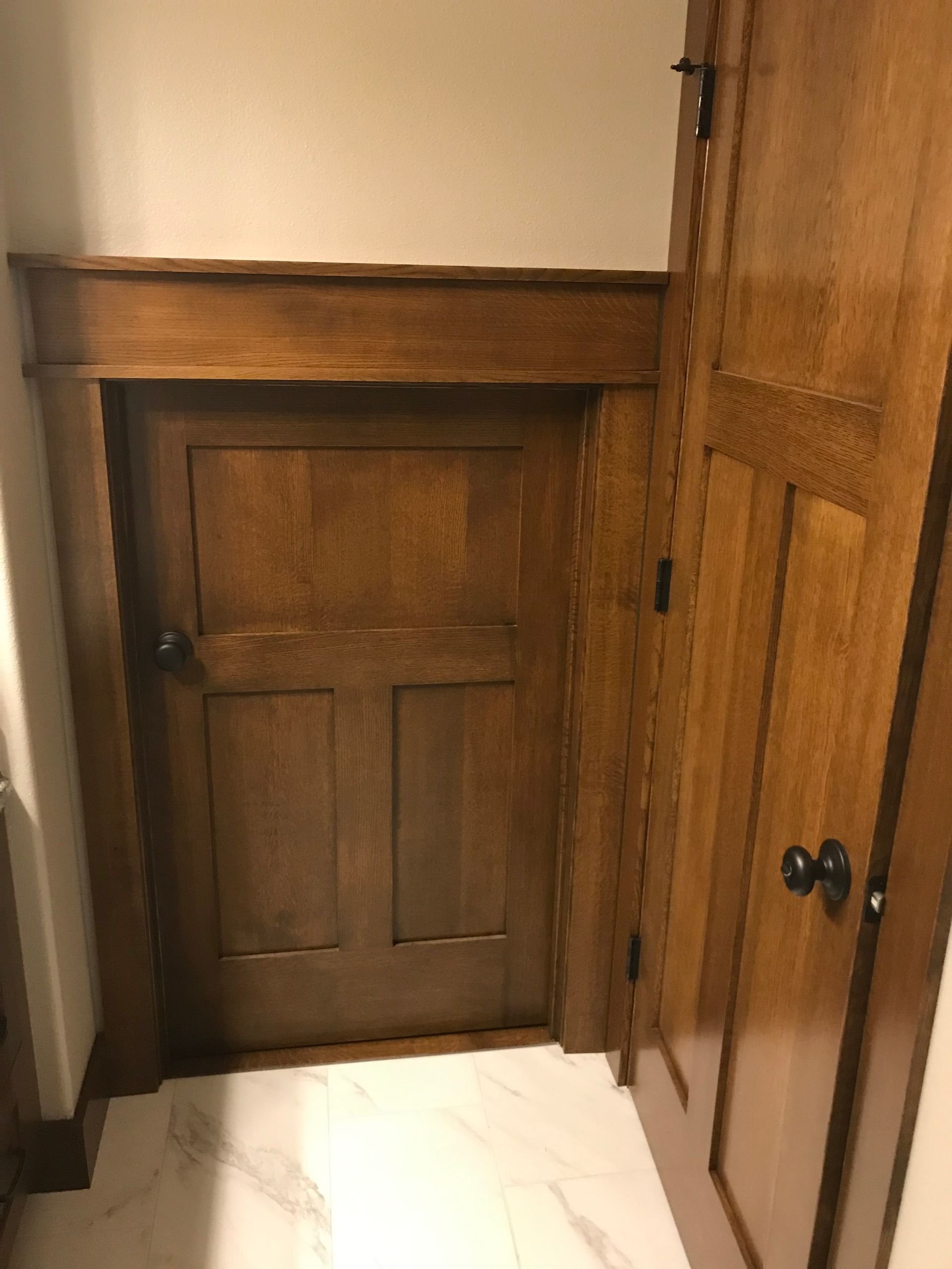 Small wooden door at the end of a narrow hallway with built-in closets and white tile floor.