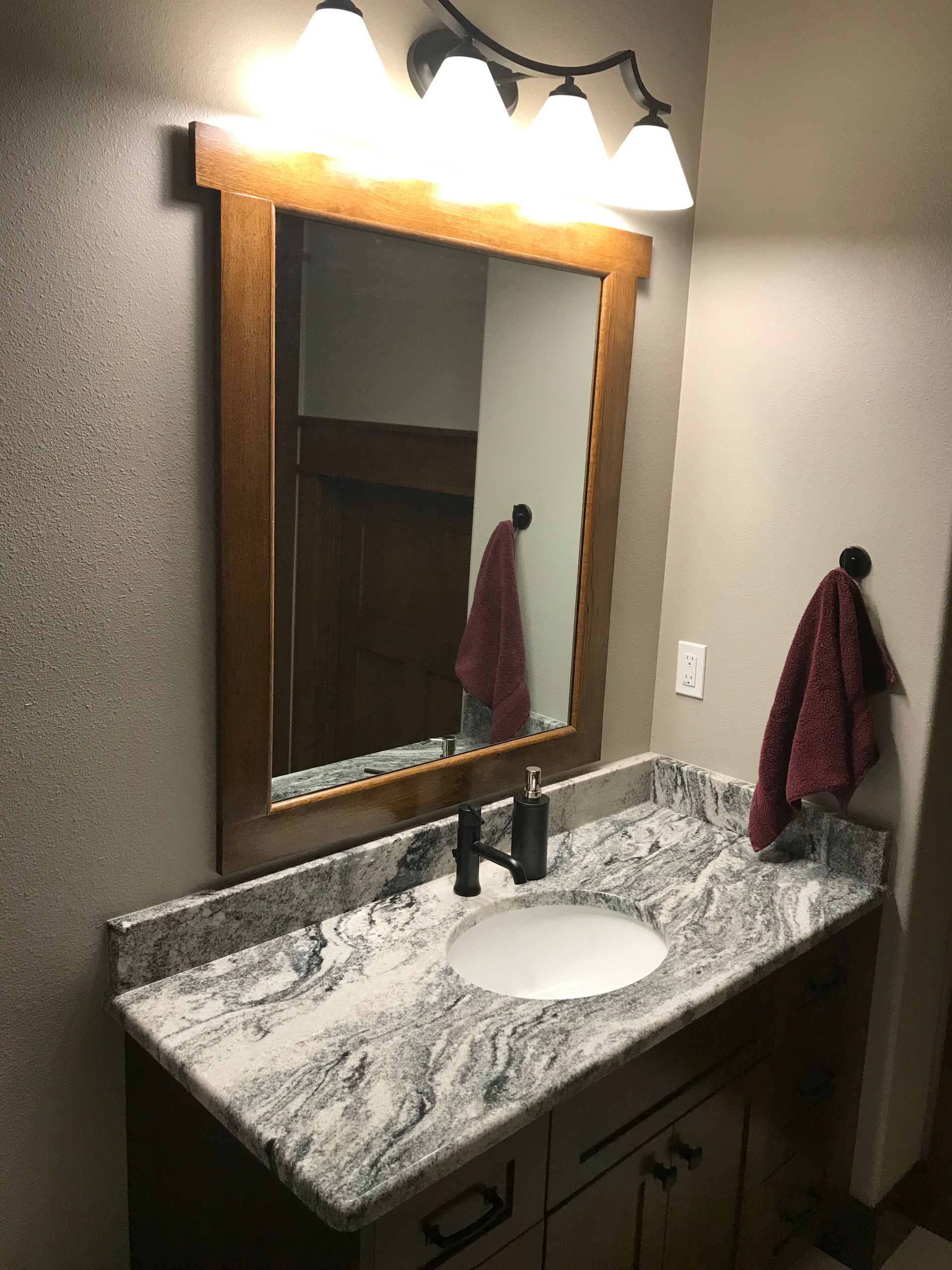 Bathroom vanity with granite sink, large mirror, and wall sconce lighting above the countertop.