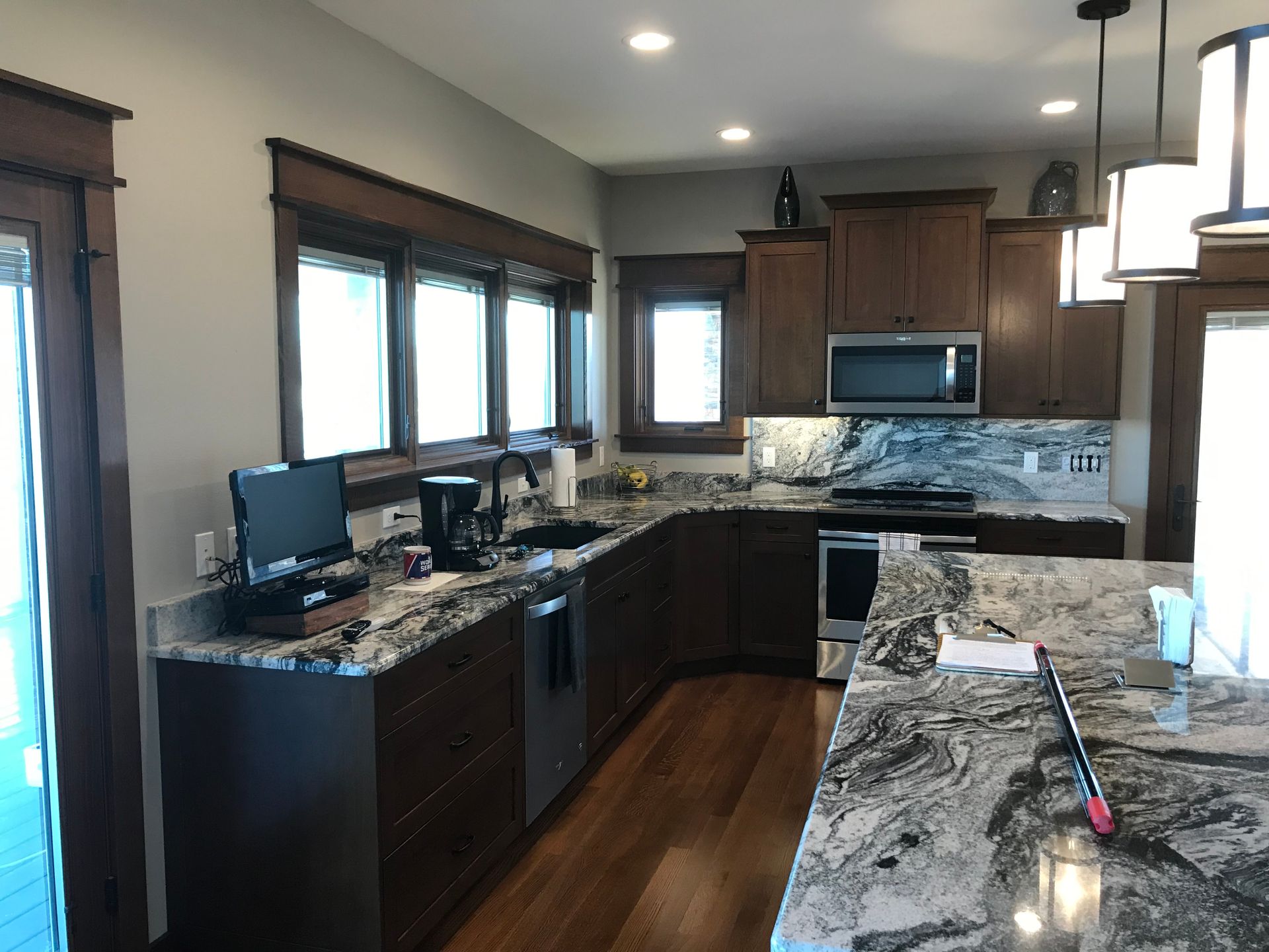 Modern kitchen with dark wood cabinets, granite counters, stainless appliances, and three windows over the sink.