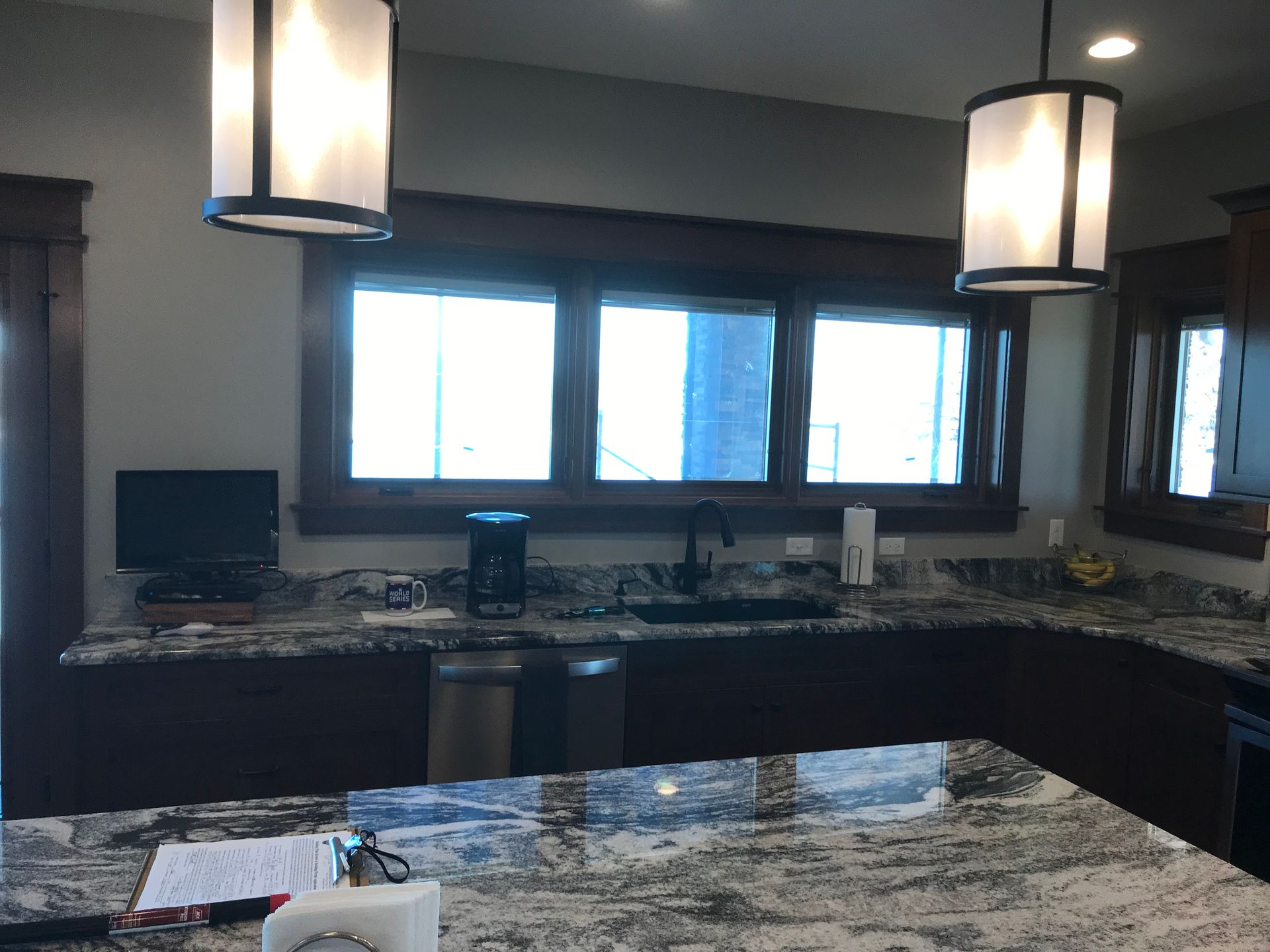 Modern kitchen with granite island, dark cabinets, pendant lights, and large windows