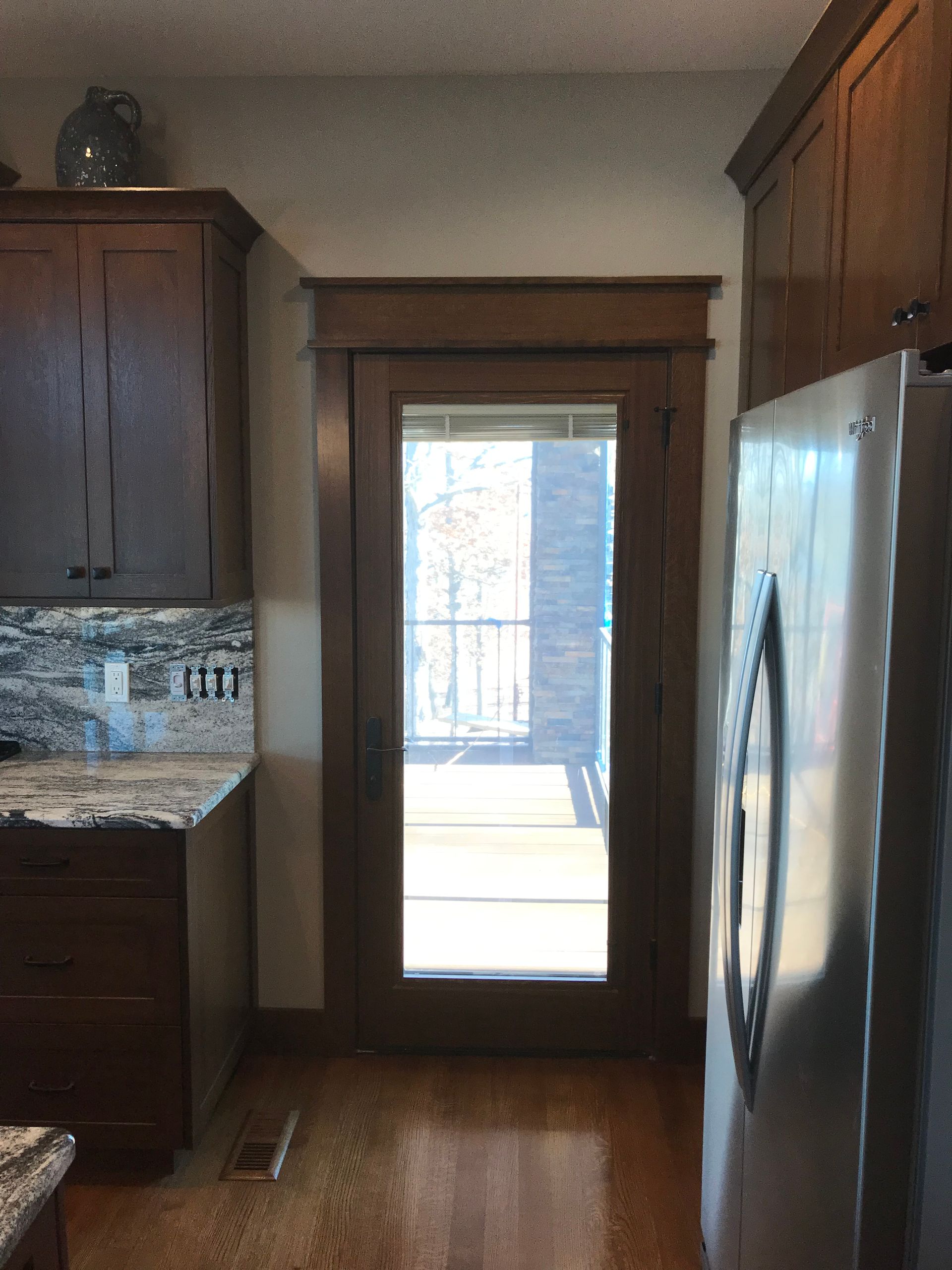 Kitchen interior with dark wood cabinets, stainless refrigerator, and a glass door leading outside.