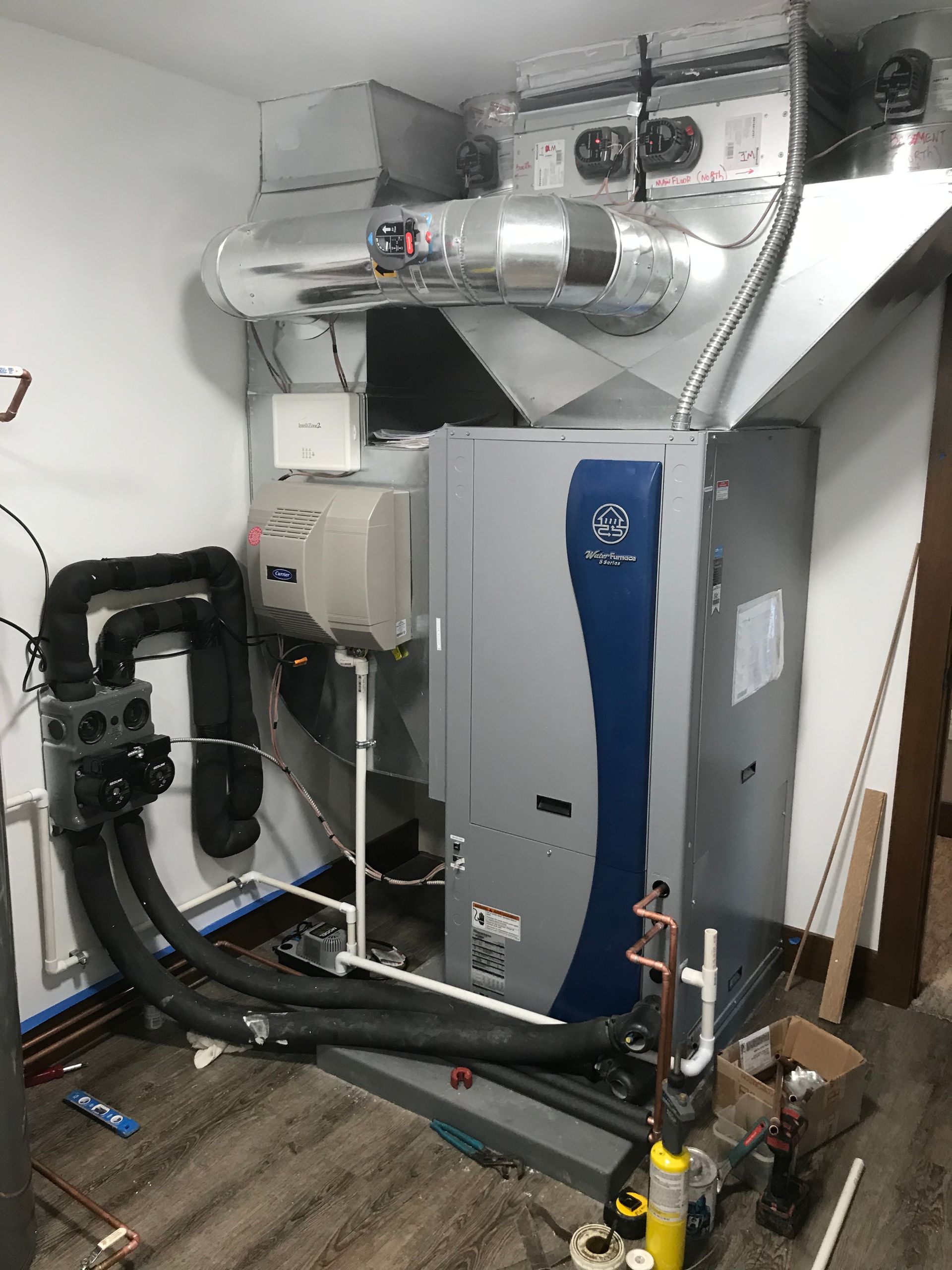 Utility room with HVAC unit, ductwork, and insulated pipes against white walls.