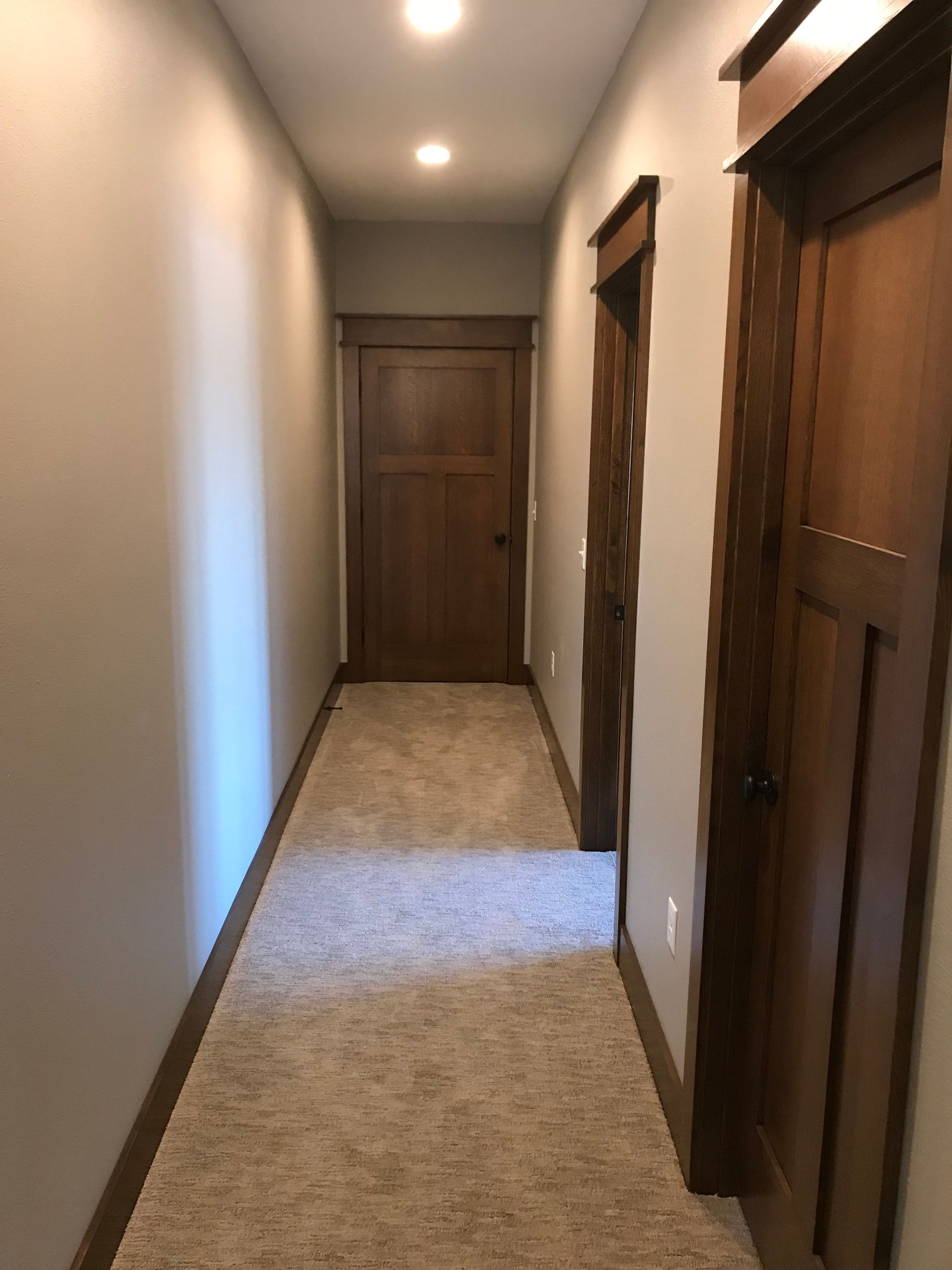 Narrow hallway with beige carpet, white walls, and wooden doors at both ends.