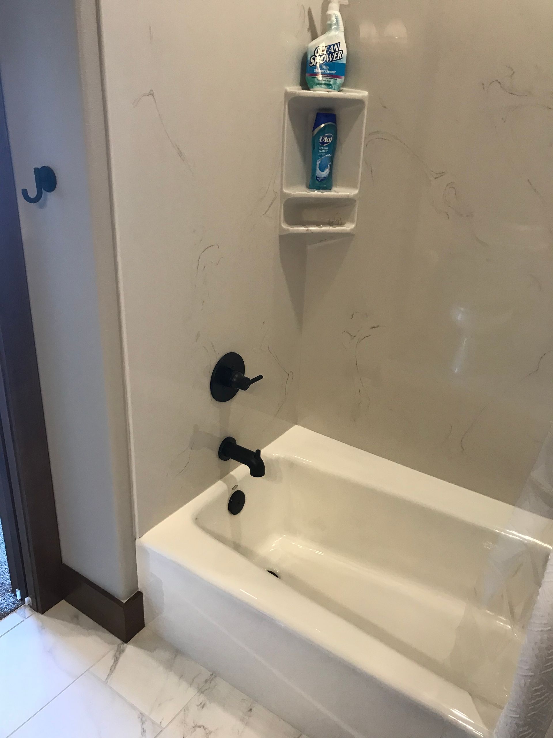 Bathtub shower with black fixtures, wall shelf, and decorative bottles in a small bathroom