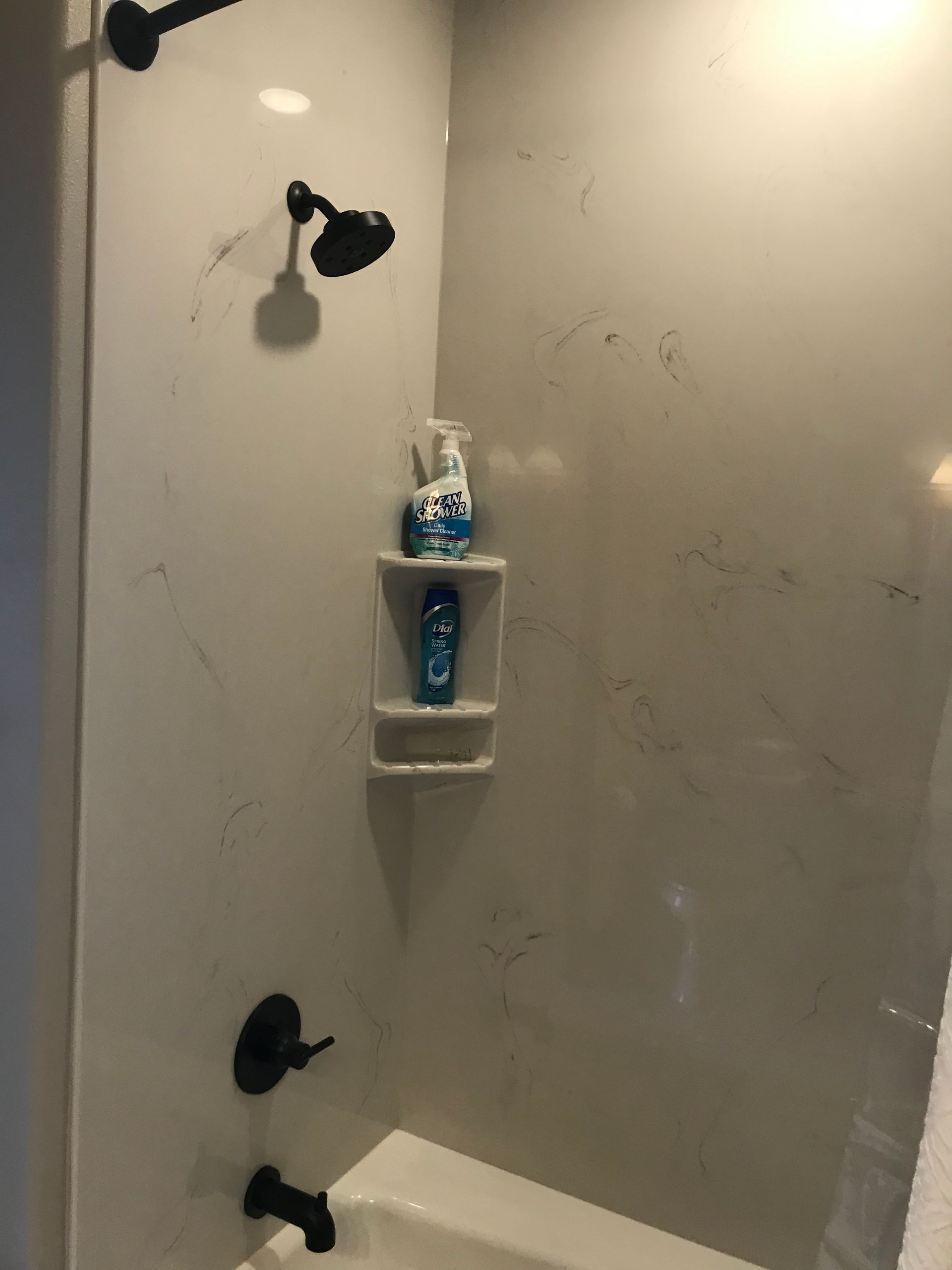 Small white shower stall with black fixtures and a wall shelf holding toiletries.