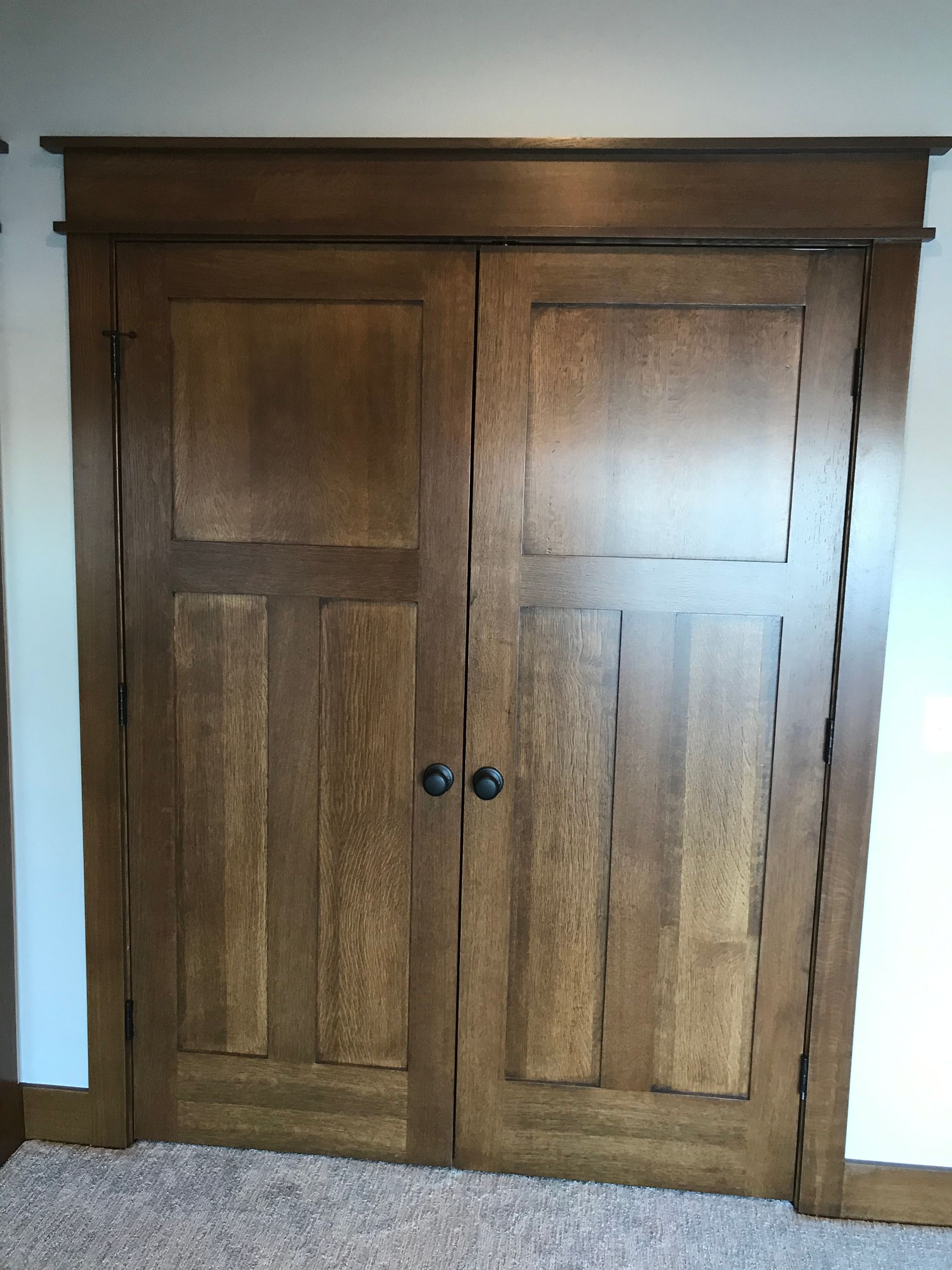 Wooden double closet doors with dark knobs in a hallway or room.
