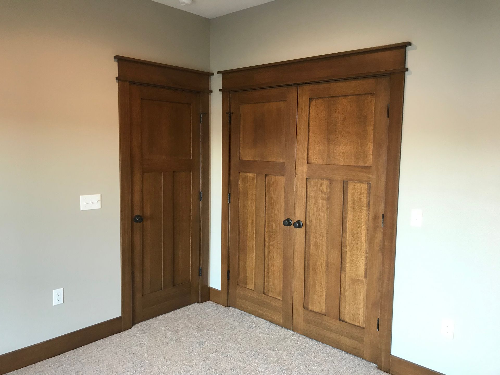 Corner of a room with two wooden closet doors and beige carpet