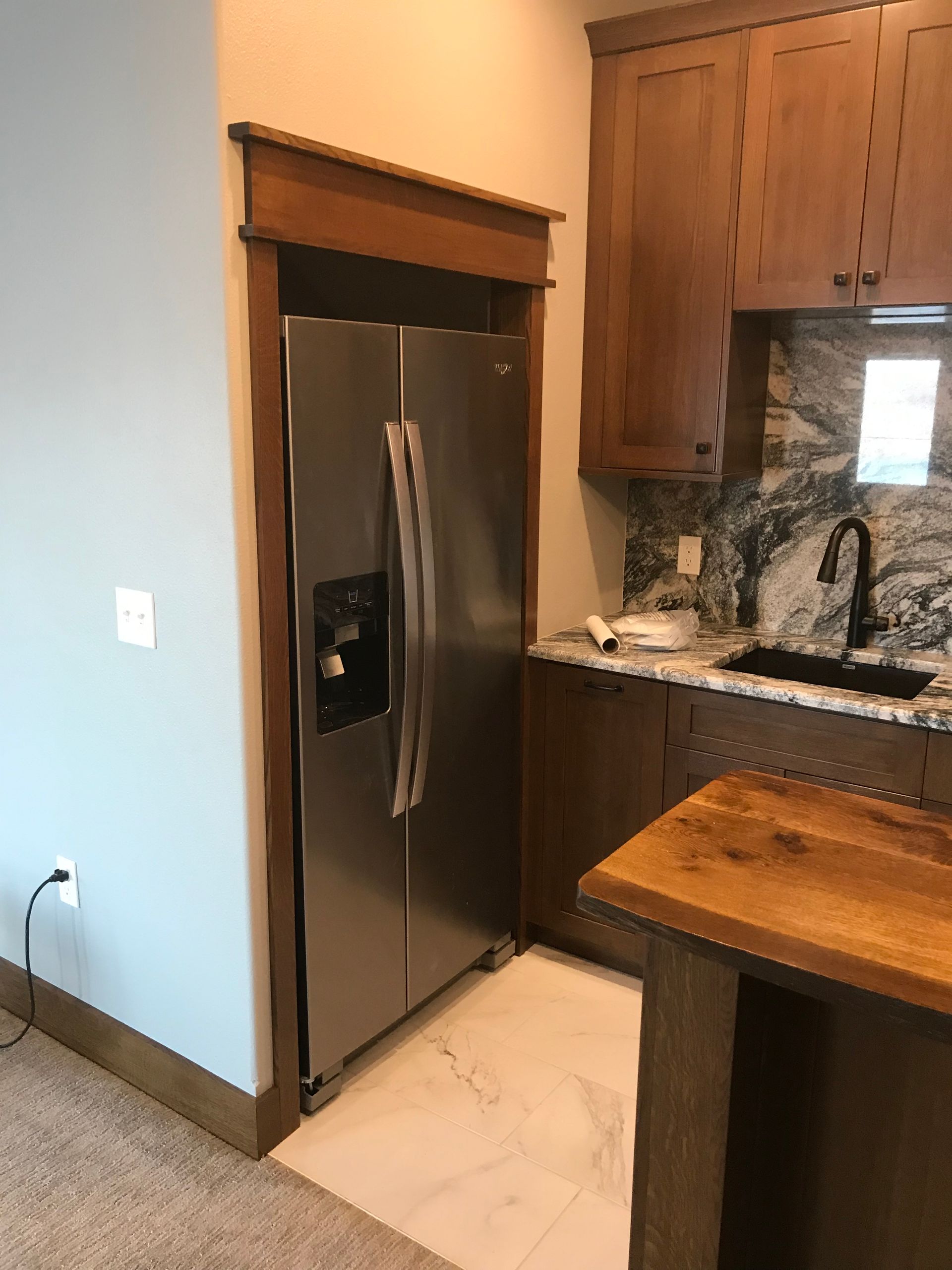 Kitchen with stainless steel fridge, granite counters, wood cabinets, and a small island.