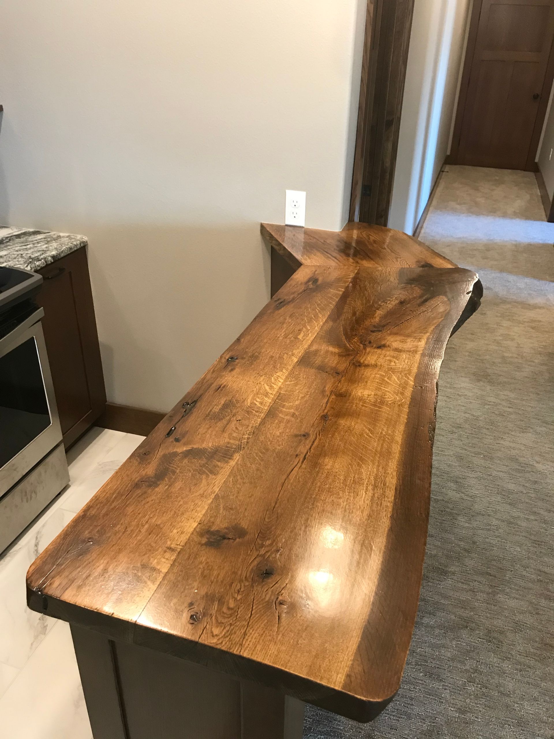 Rustic live-edge wooden console table in a hallway, with dark legs and a glossy finish.