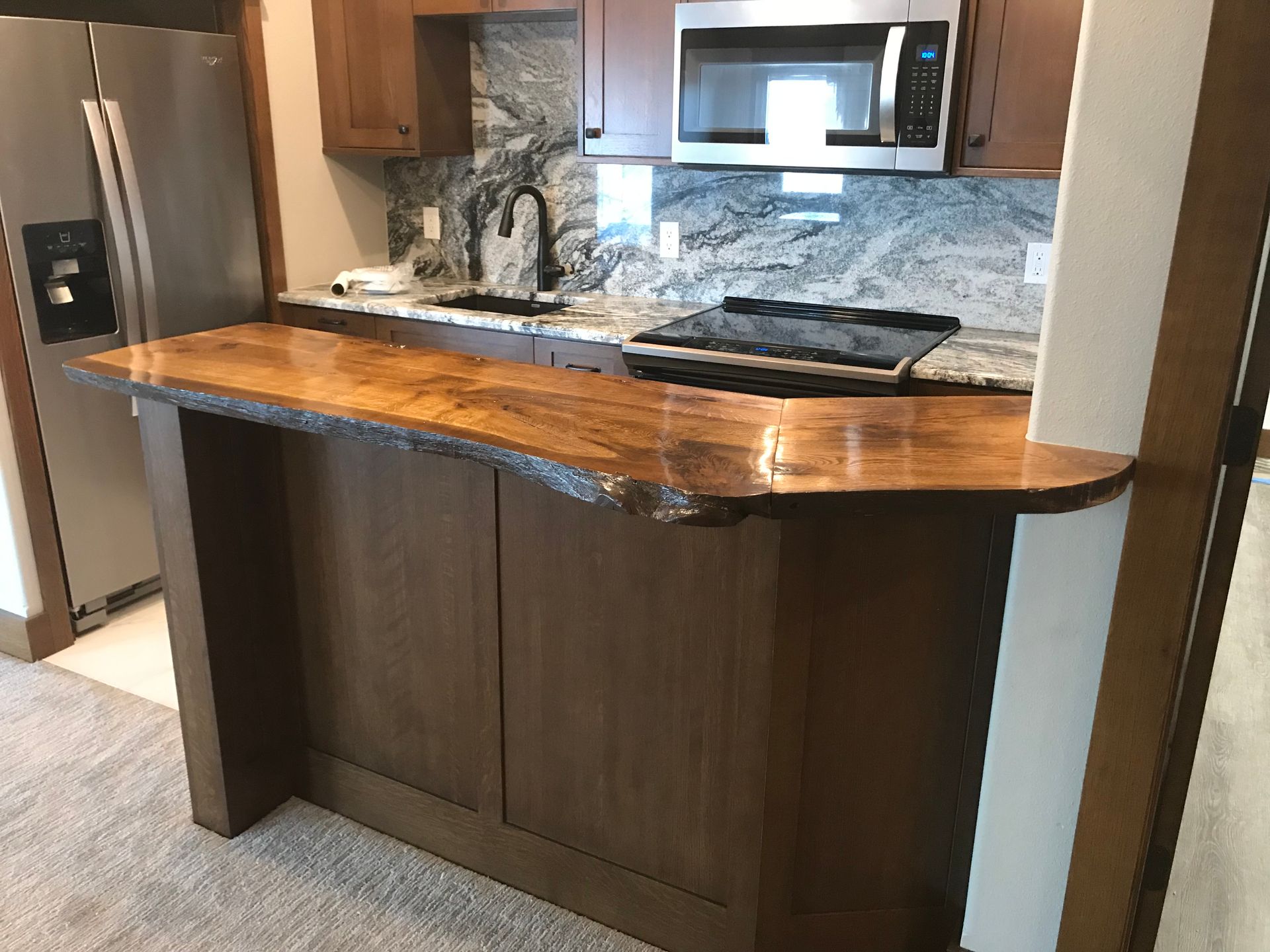 Modern kitchen island with wooden countertop, stainless steel appliances, and dark wood cabinets