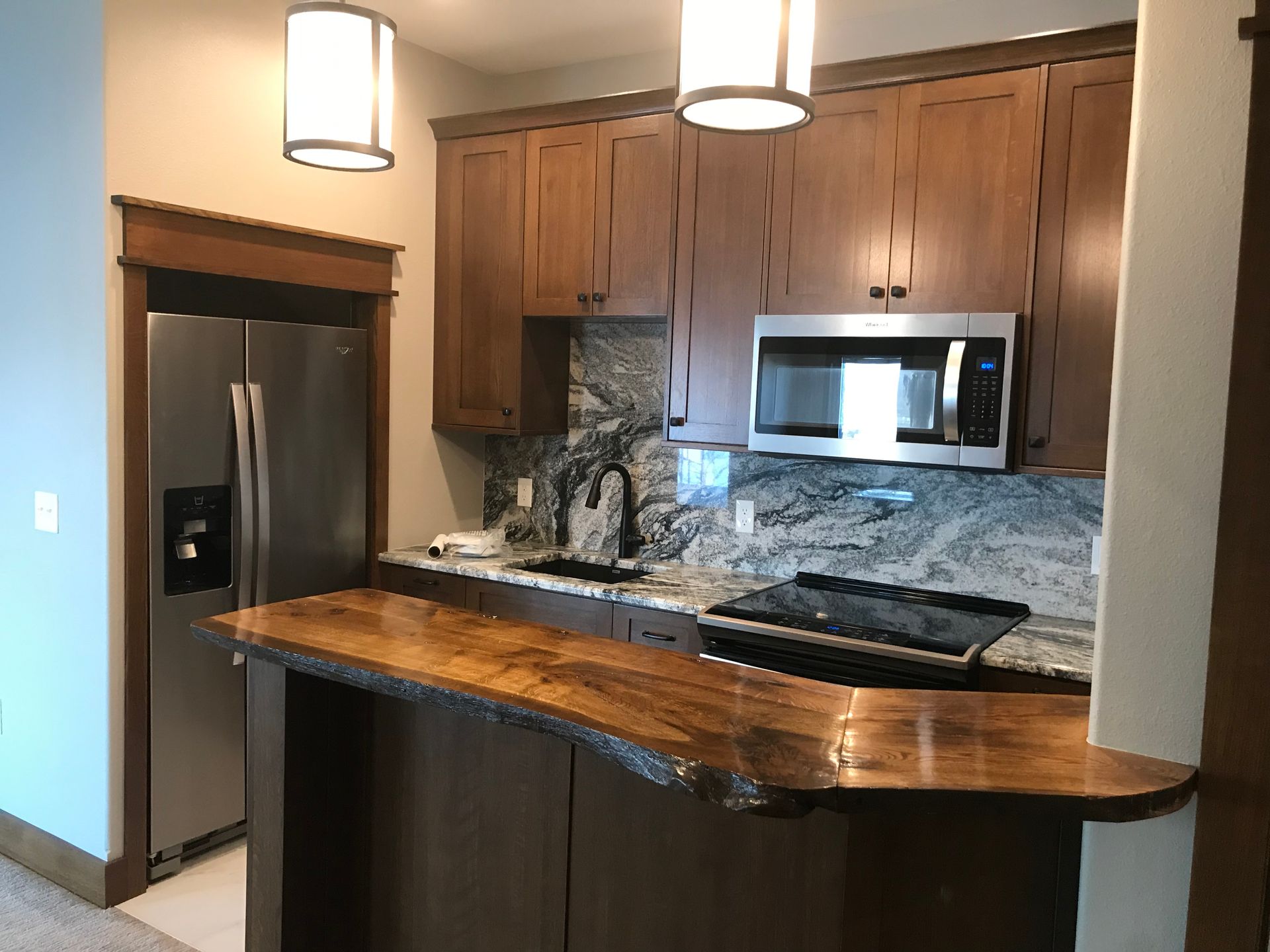 Modern kitchen with wood cabinets, granite island, stainless steel appliances, and pendant lights.