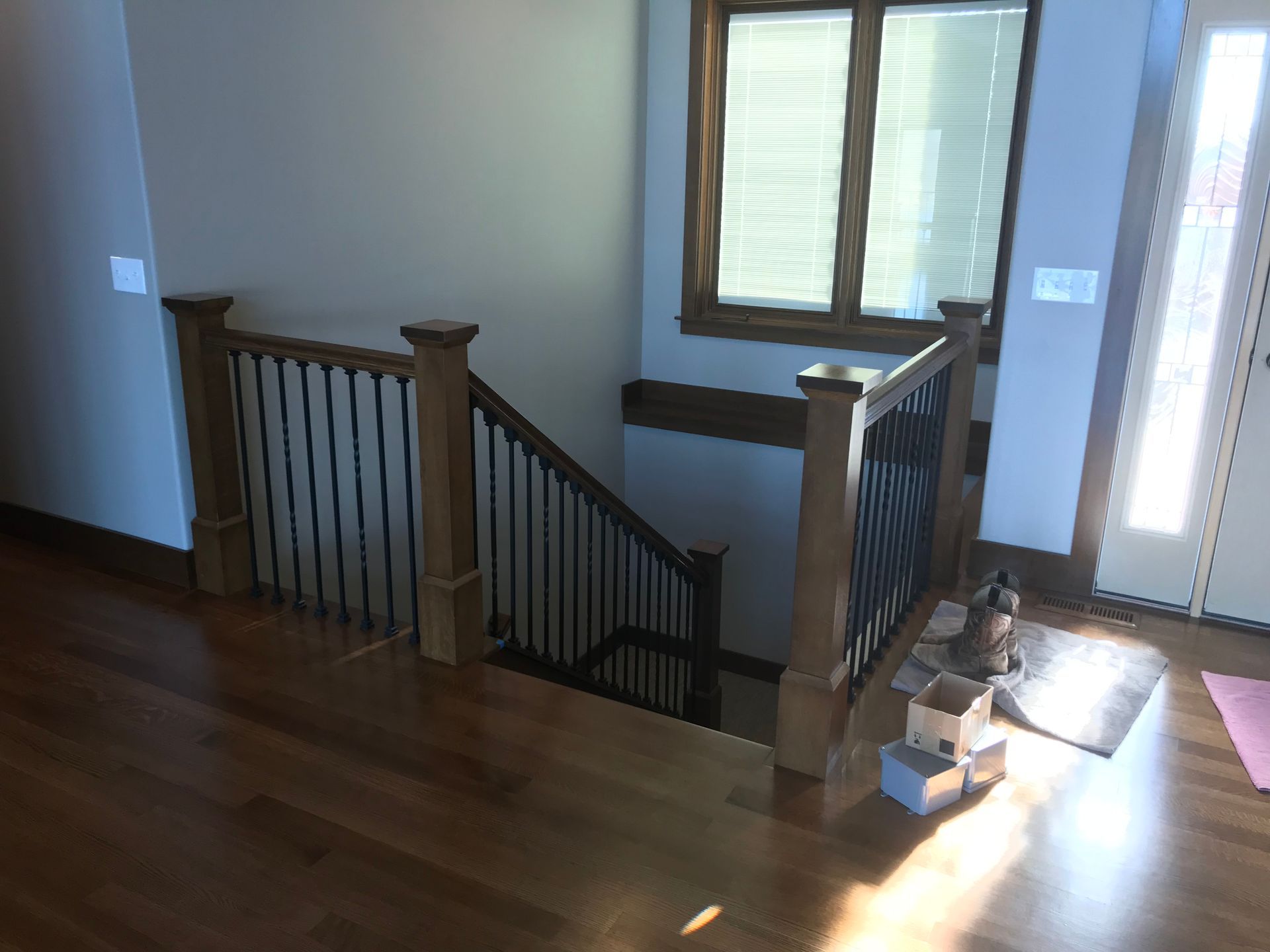 Staircase landing with dark wood railing, window, and sunlight on hardwood floor