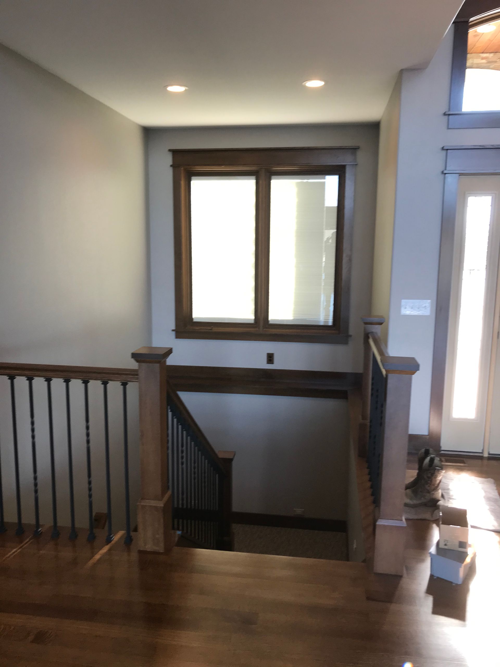 Interior stair landing with wooden railing, window, and doorway in a softly lit hallway