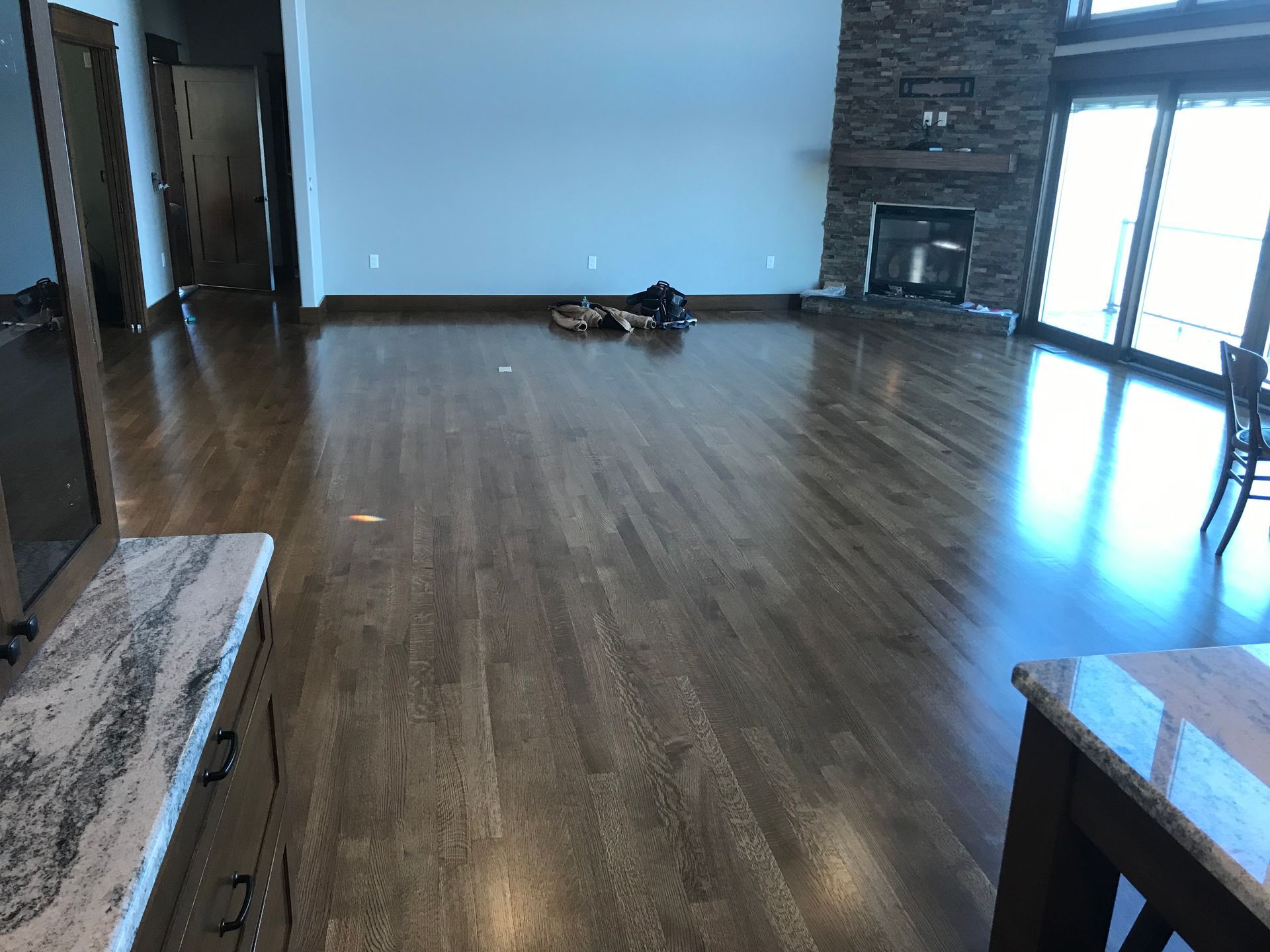 Empty living room with hardwood floors, stone fireplace, and bright windows along the right wall