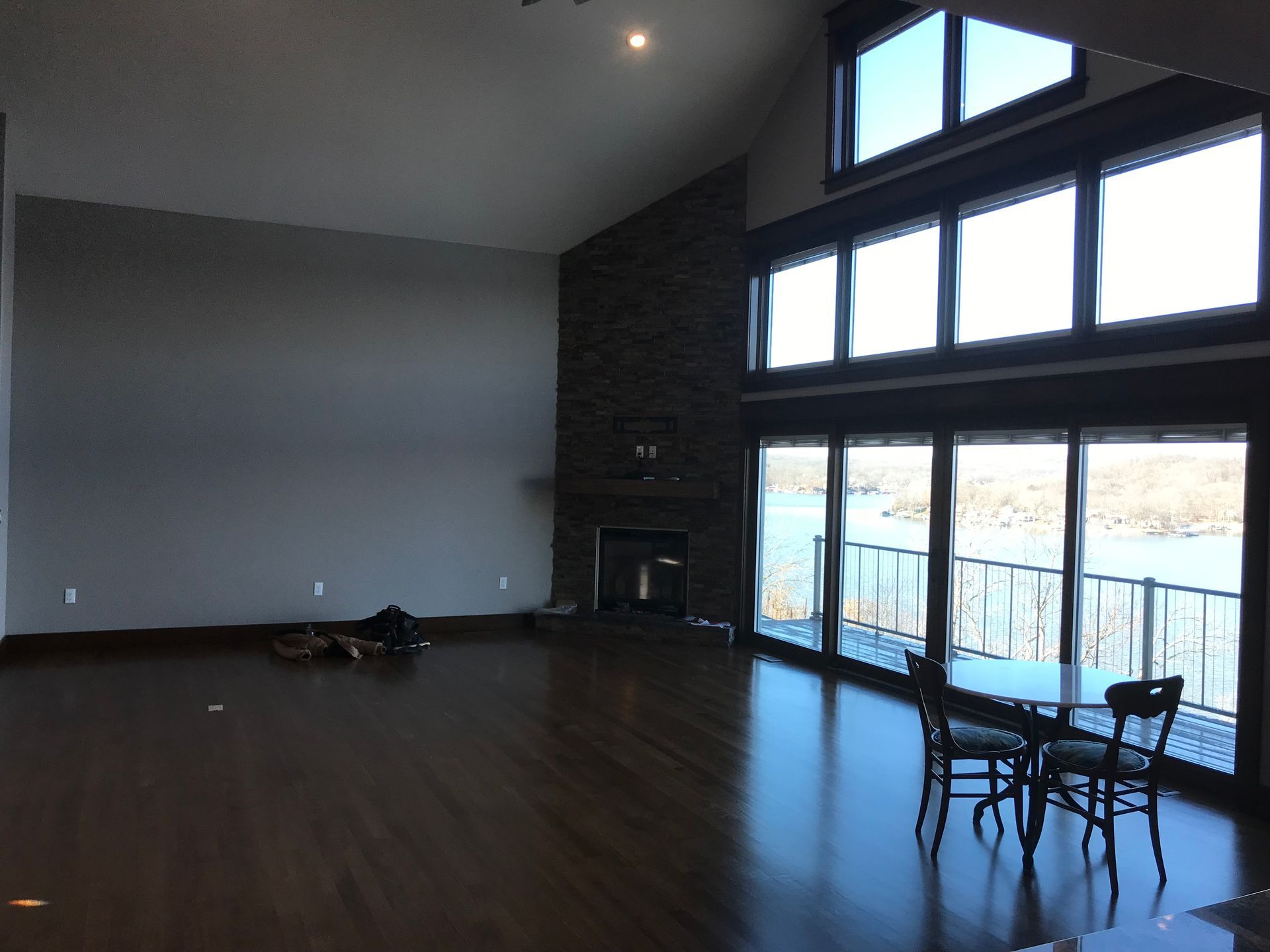 Spacious living room with dark floors, tall windows, and a small table near the glass doors.