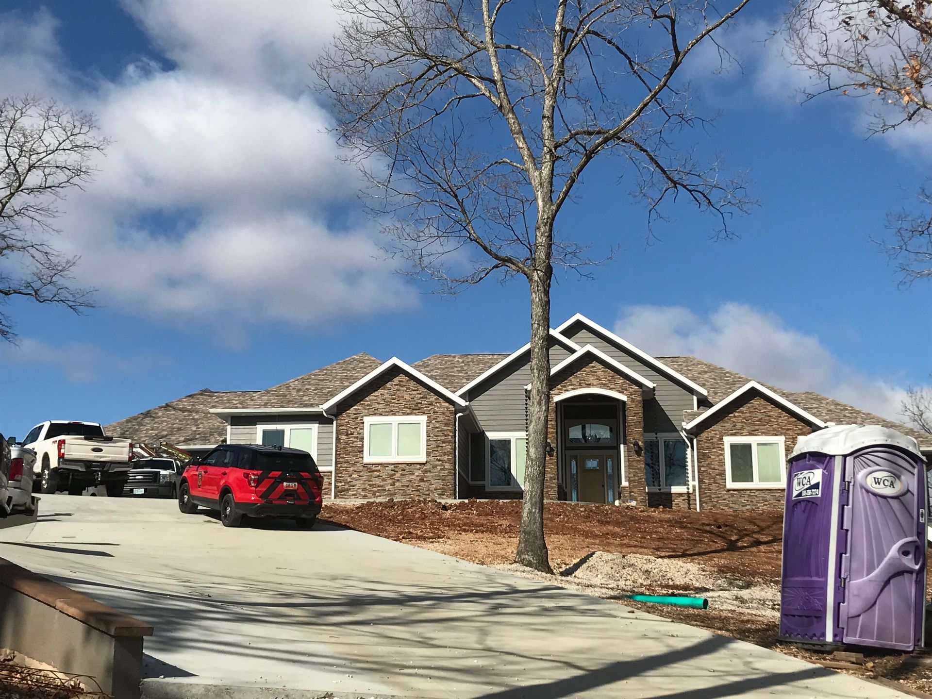 Single-story house with a red car in the driveway and two purple portable toilets on the right.