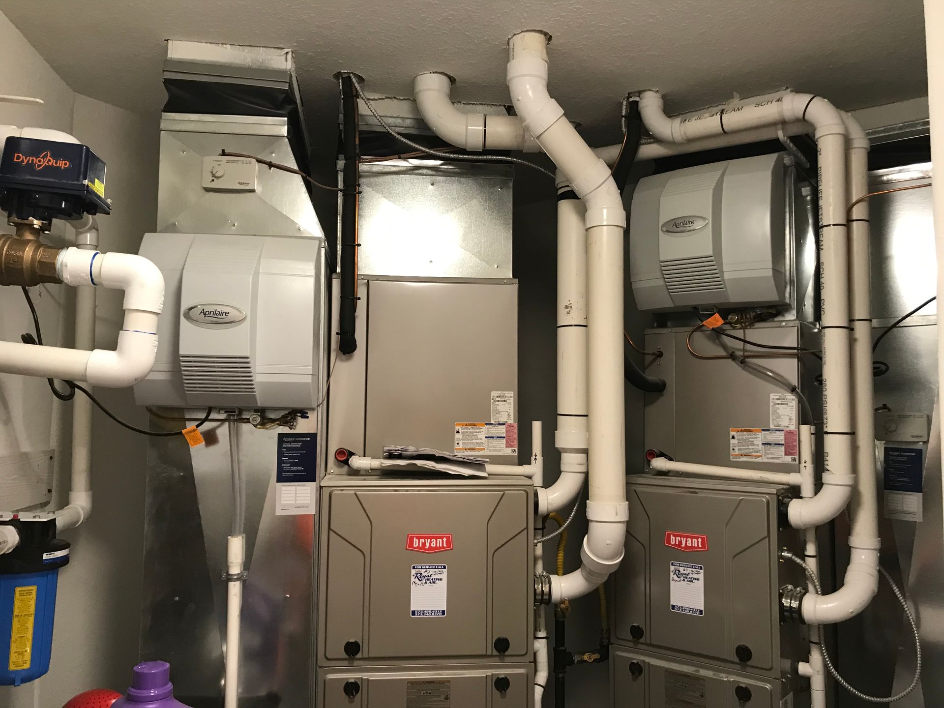 Mechanical room with HVAC units, ducts, and white piping against a gray wall.