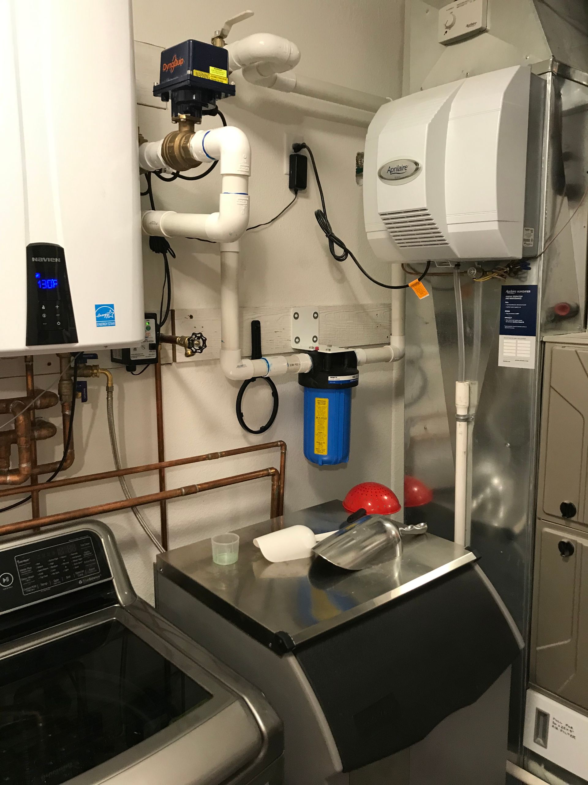 Commercial kitchen prep area with stainless steel equipment, ventilation hood, pipes, and cleaning supplies.