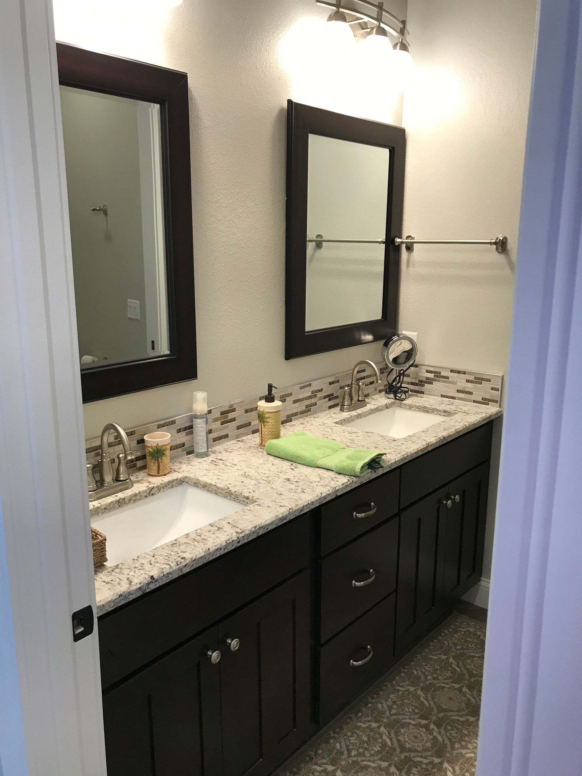Bathroom vanity with two mirrors, dark cabinets, and a white countertop sink.