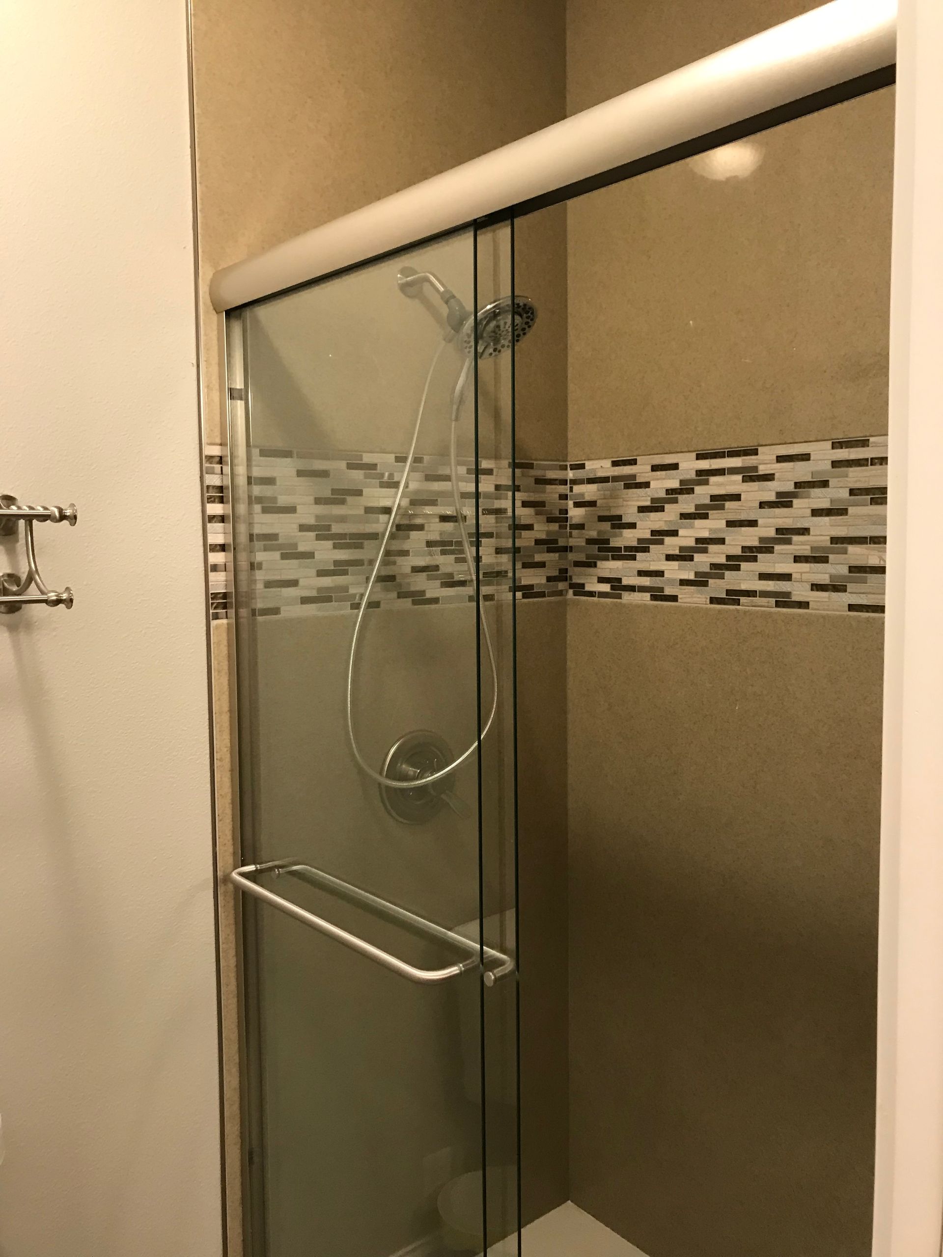 Glass shower enclosure with chrome handle and showerhead in a beige tiled bathroom