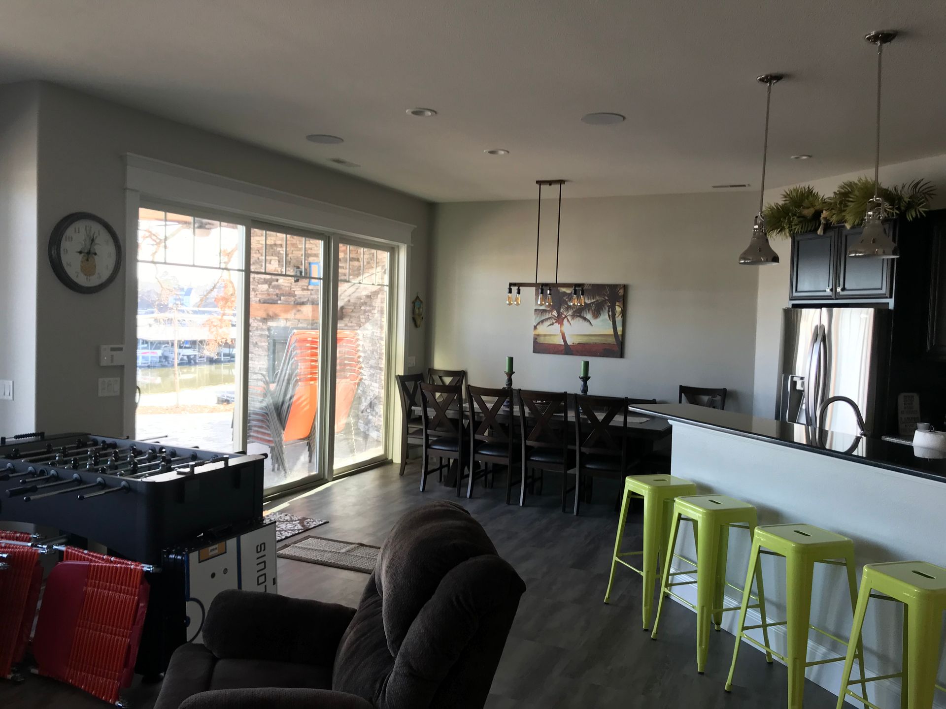 Modern open-plan living room with sliding glass doors, dining table, and kitchen island with green stools