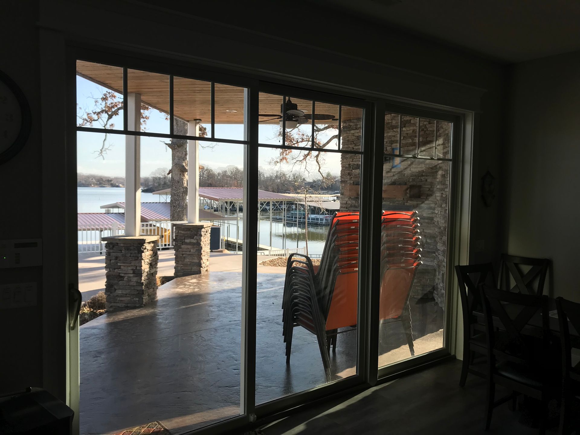 Indoor view of a snowy patio through large glass doors, with a chair and table outside.